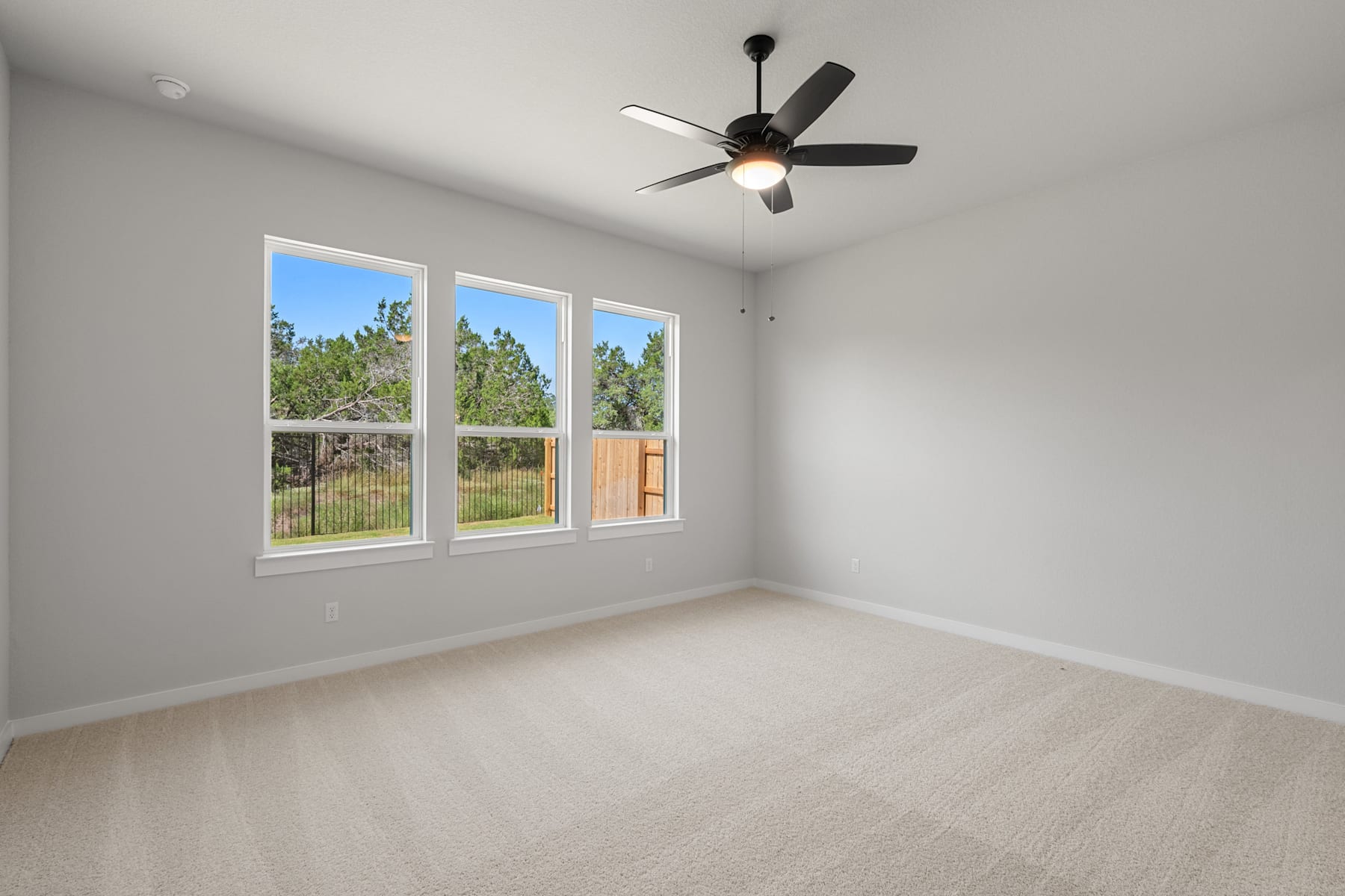 A spacious, well-lit room with a ceiling fan and large windows overlooking a wooded area outside.