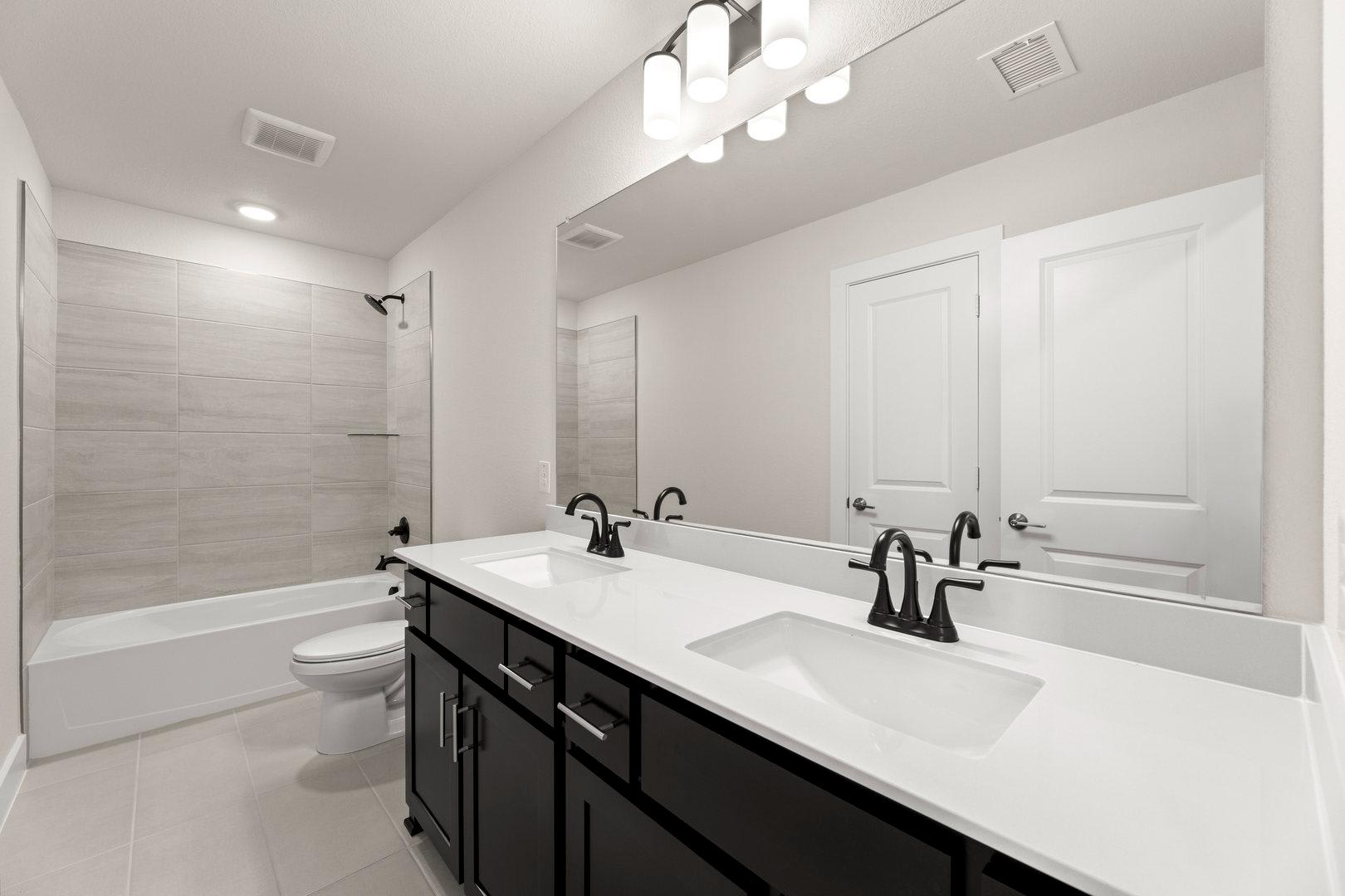 A modern and minimalist bathroom with a double vanity, white countertops, and black cabinetry, complemented by a large mirror and recessed lighting.
