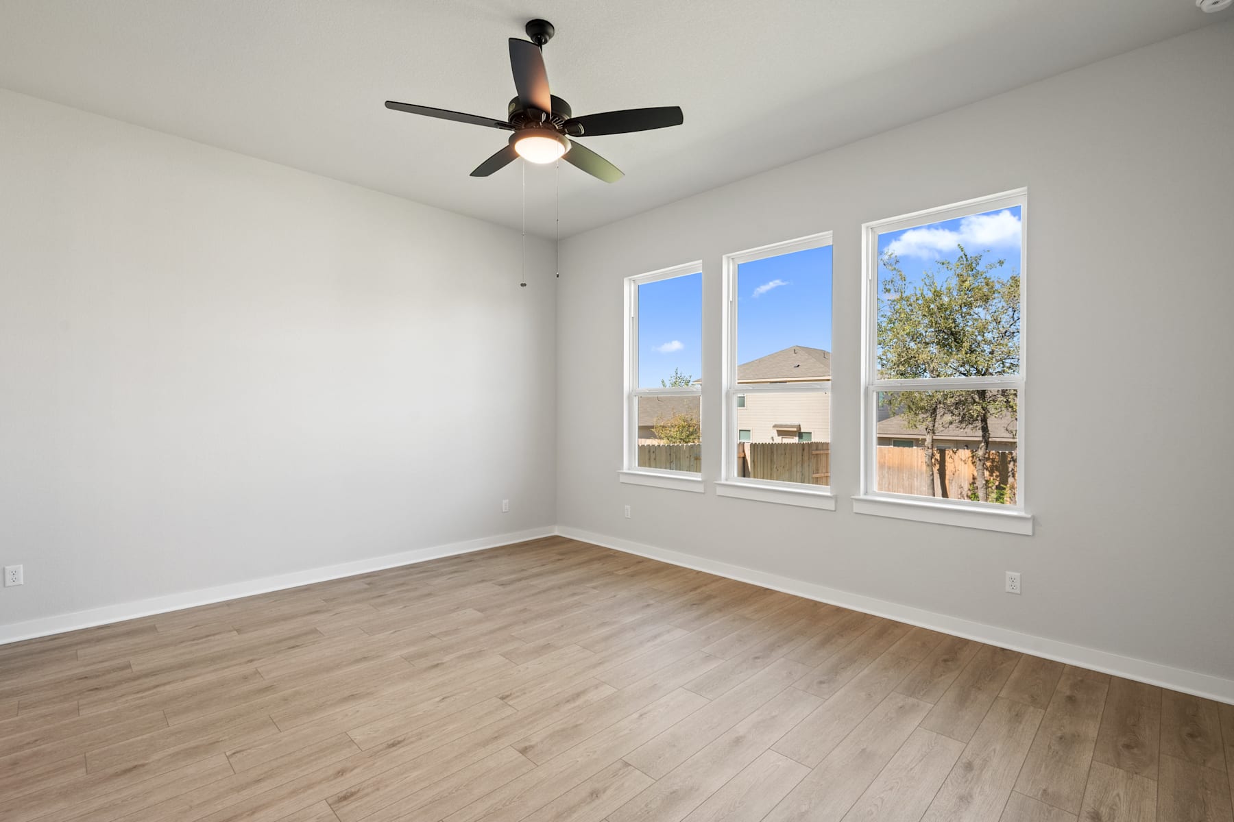 A spacious, well-lit room with a ceiling fan and large windows overlooking a scenic outdoor area.