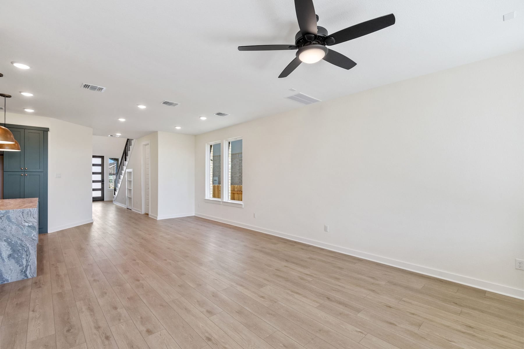 A spacious, well-lit room with a ceiling fan, hardwood floors, and a minimalist design aesthetic.