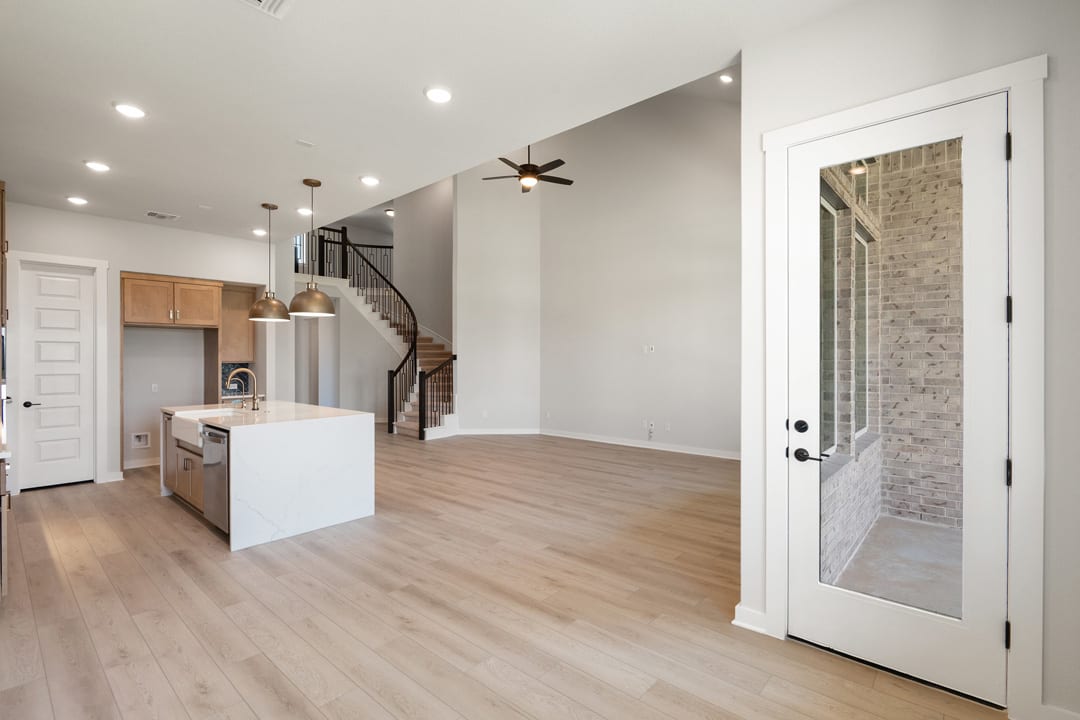 A modern, open-concept kitchen and living space with hardwood floors, white walls, and a spiral staircase leading to an upper level.
