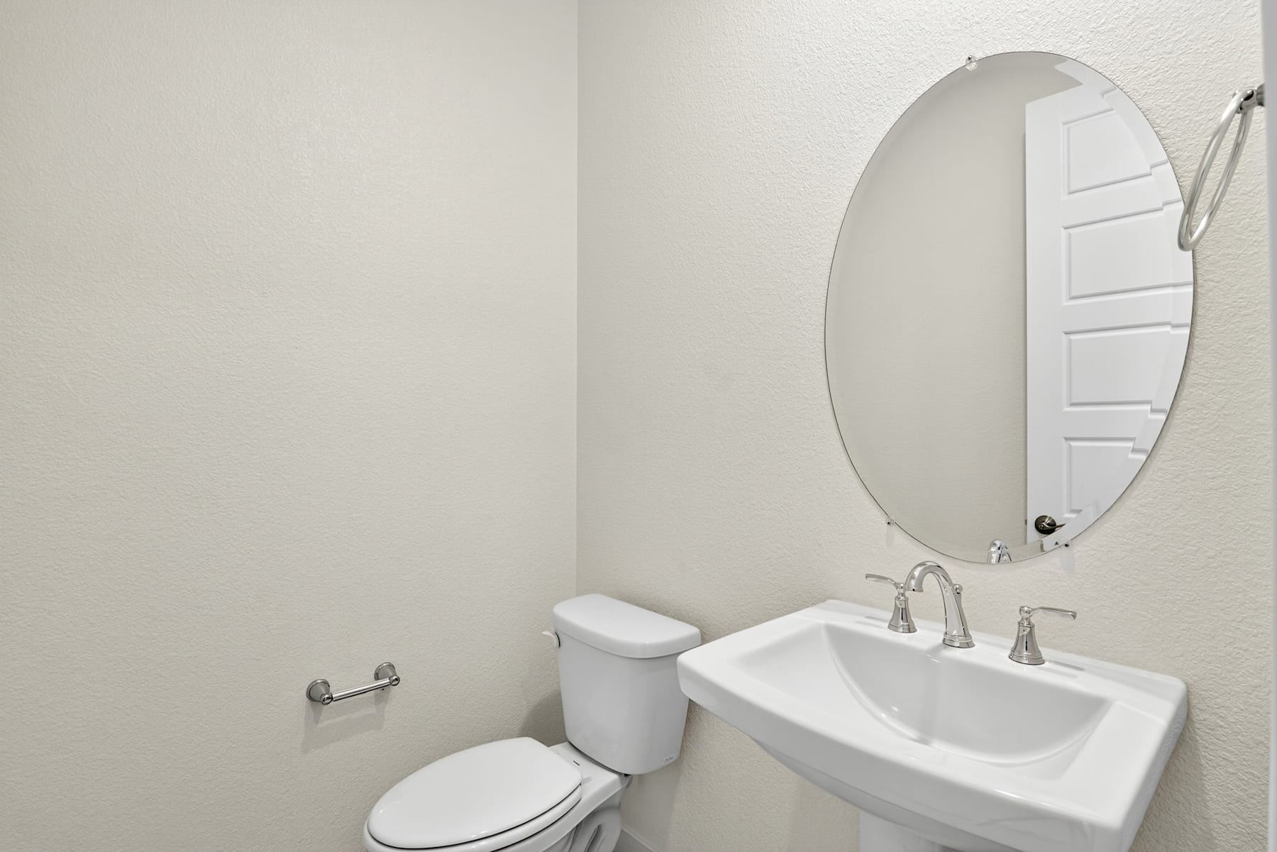 A simple and clean bathroom with a white toilet, a pedestal sink, and an oval mirror on the wall.