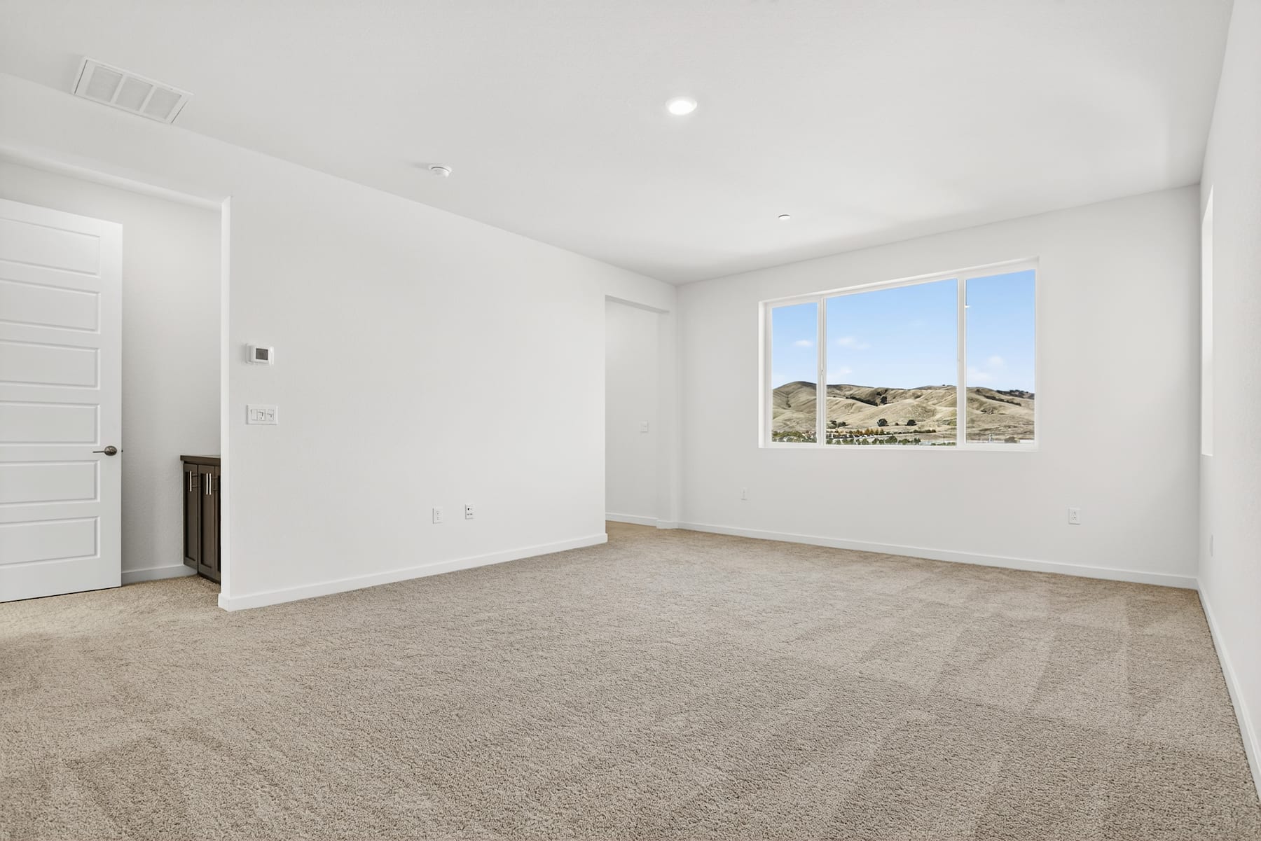 An empty, spacious room with white walls, a large window overlooking a scenic outdoor landscape, and a carpeted floor.