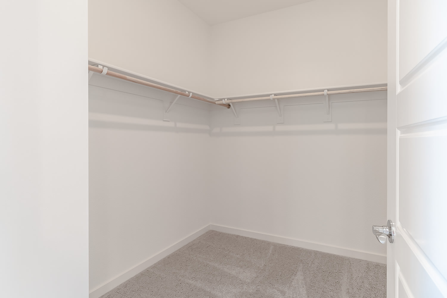 A small, empty closet with white walls and a gray carpeted floor, featuring a metal clothing rod installed along the top.