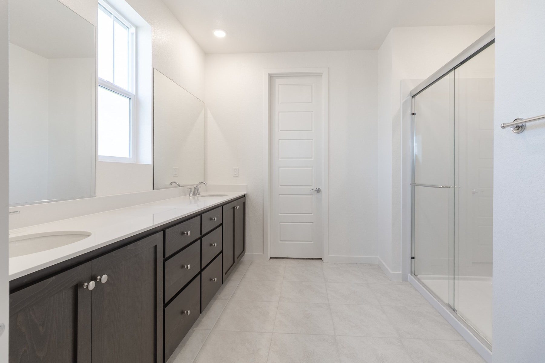 A modern and spacious bathroom with a large vanity, a mirror, and a glass shower enclosure, all set against a bright and airy backdrop.