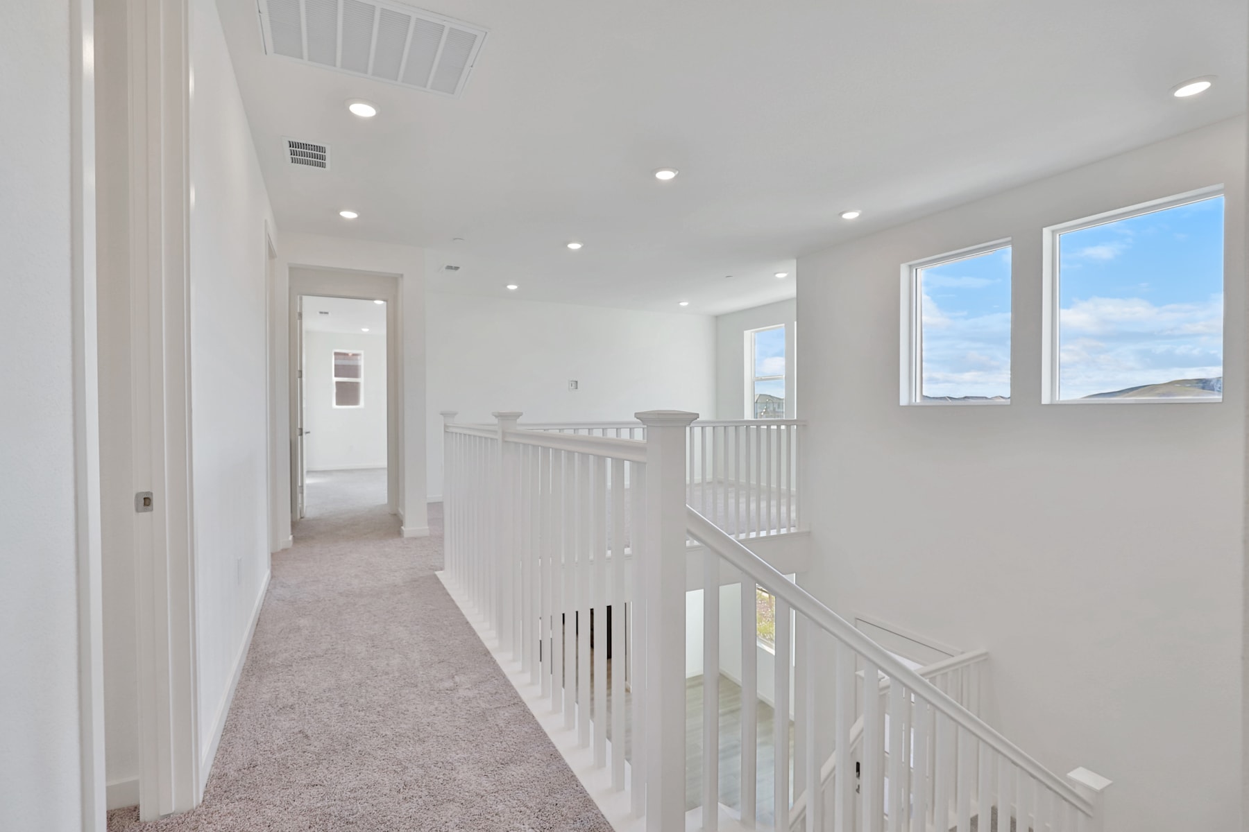 A bright, airy hallway with white walls, a carpeted floor, and a staircase with white railings leading to the upper level.