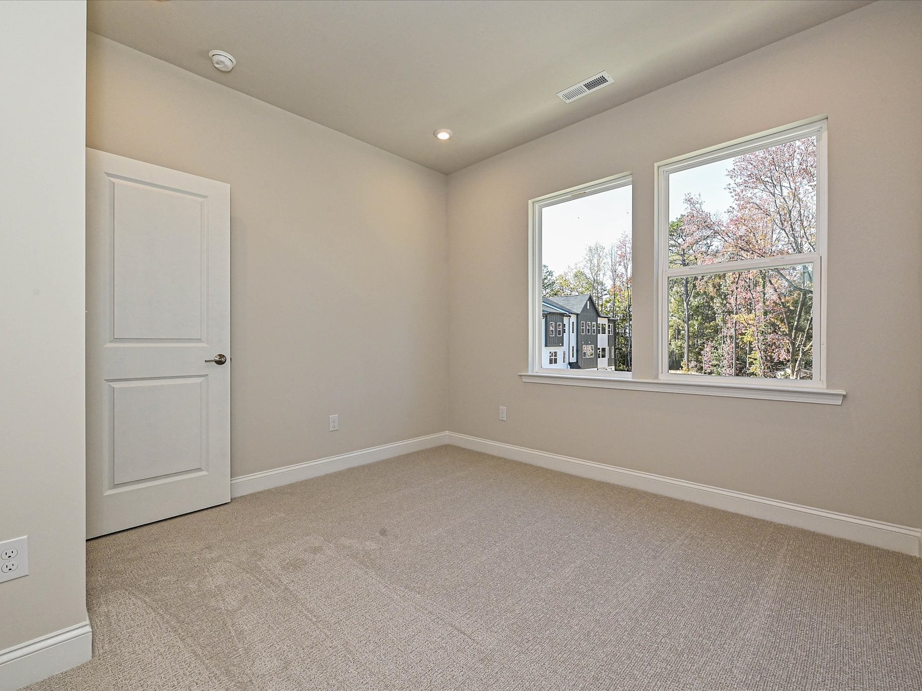 A spacious, well-lit room with a large window overlooking a wooded area, featuring a neutral color scheme and clean, minimalist design.