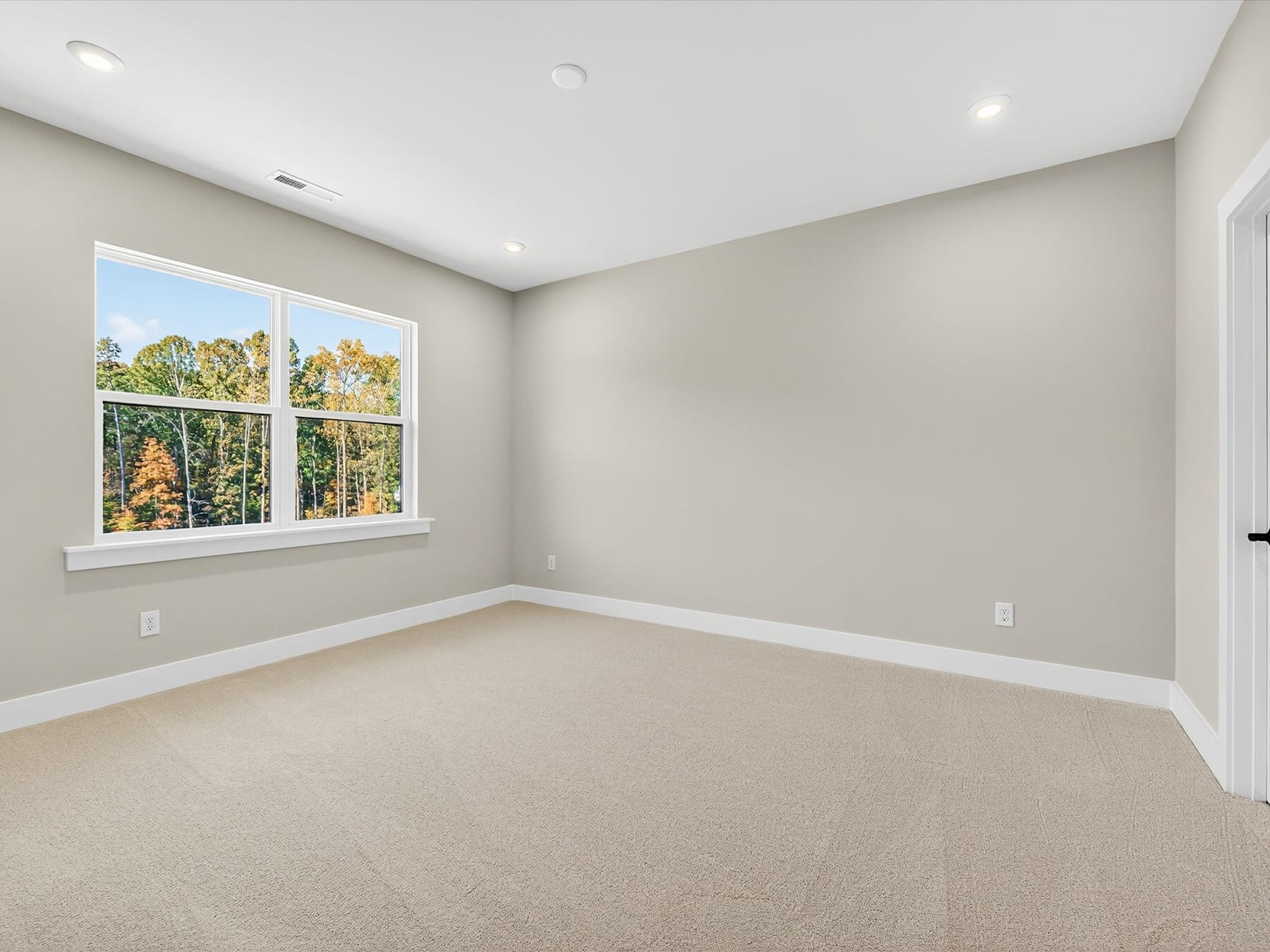A spacious, well-lit room with large windows overlooking a scenic outdoor landscape, featuring a neutral-toned color scheme and plush carpeting.