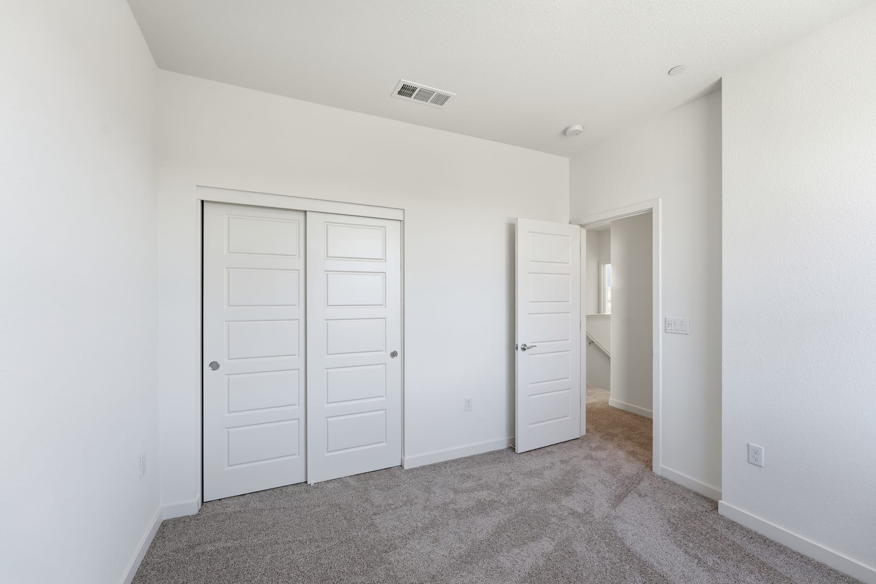 A spacious, minimalist room with white walls, gray carpeting, and two white doors leading to other areas of the space.