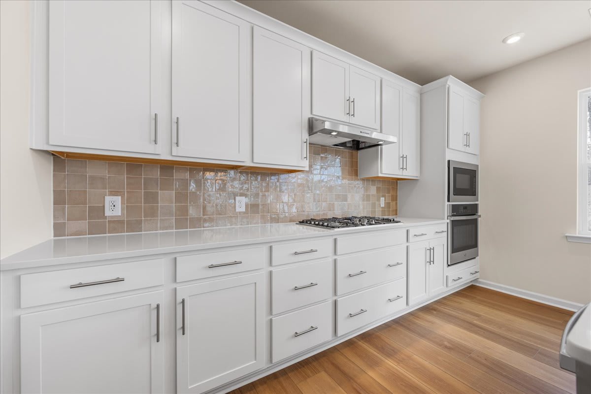 A modern, well-equipped kitchen with white cabinets, a tiled backsplash, and hardwood flooring.