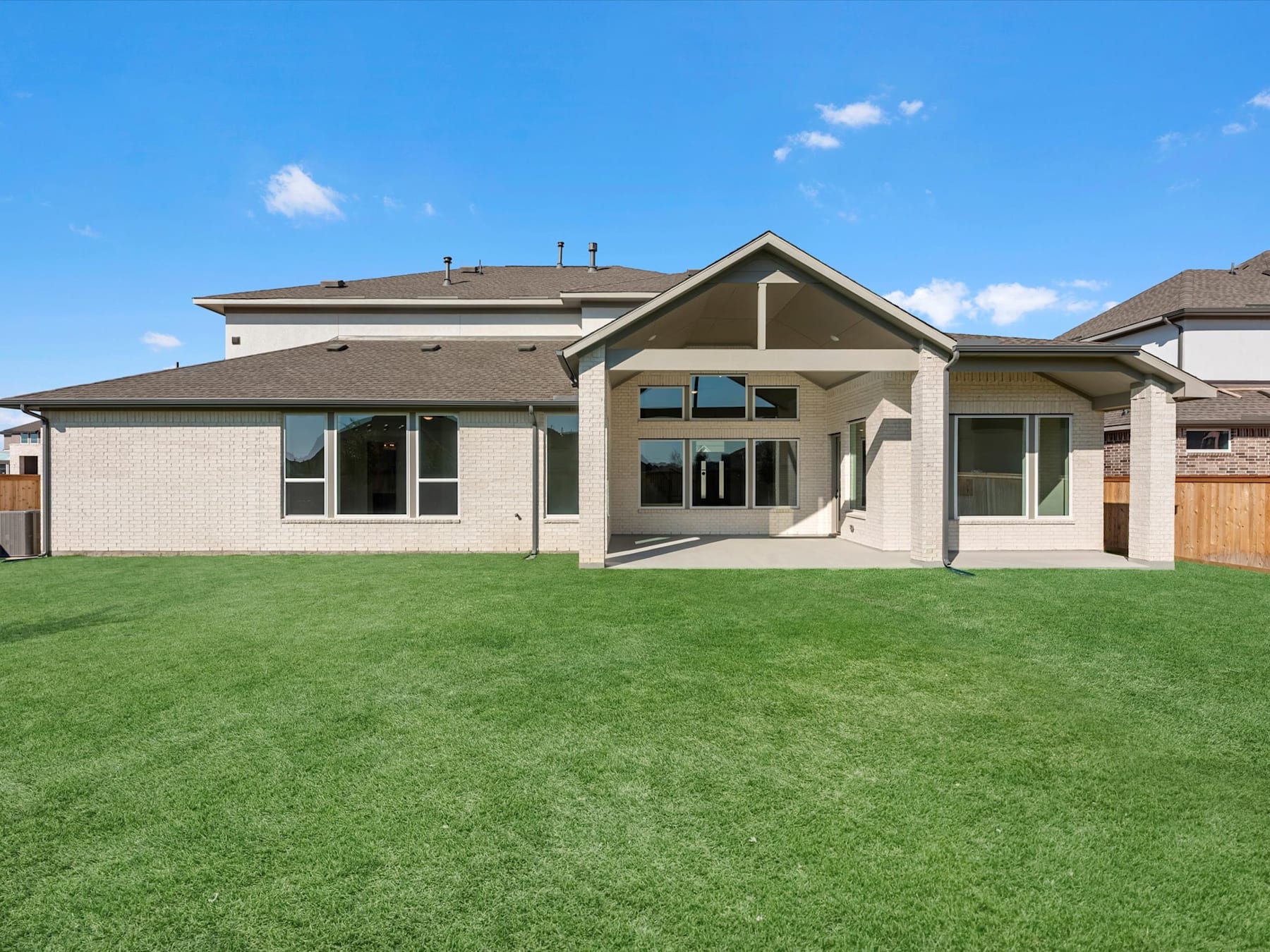 A large, modern two-story house with a well-manicured lawn in the foreground, set against a clear blue sky with a few wispy clouds.