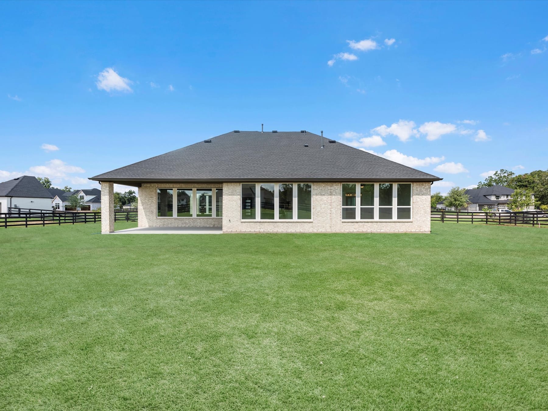 A large, single-story house with a hipped roof sits on a vast, well-manicured lawn surrounded by fences and trees in the background.