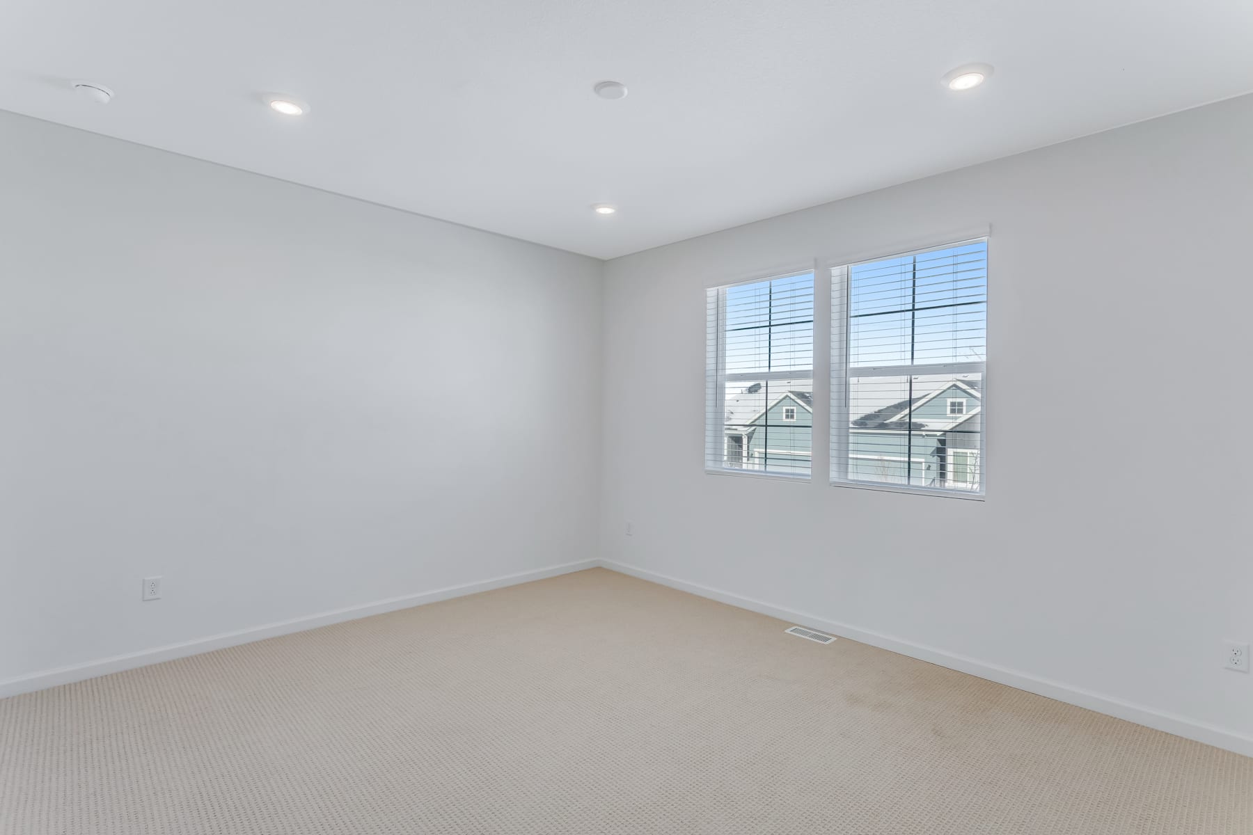 An empty, well-lit room with a large window overlooking a residential neighborhood.