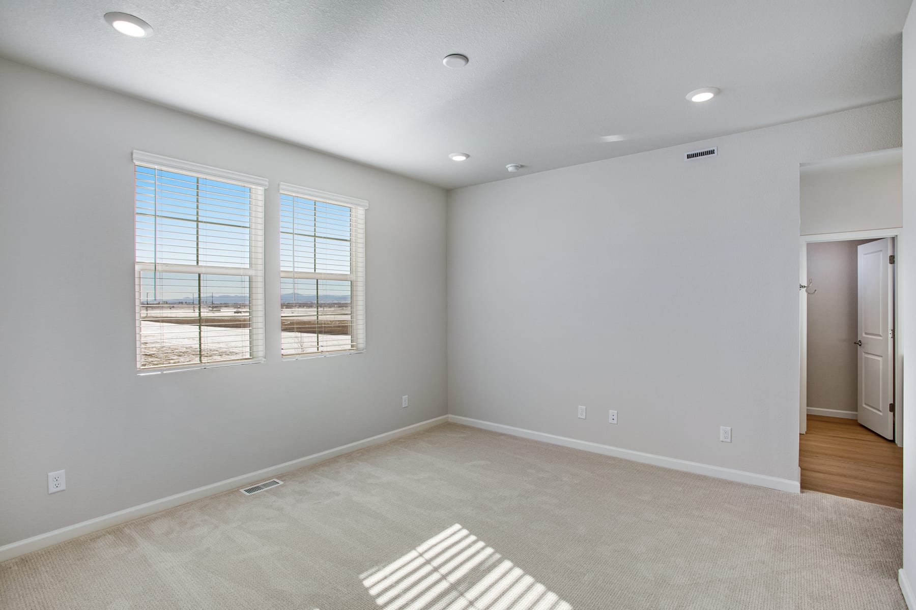 A spacious, well-lit room with large windows overlooking a scenic outdoor landscape, featuring hardwood floors and a neutral color scheme.