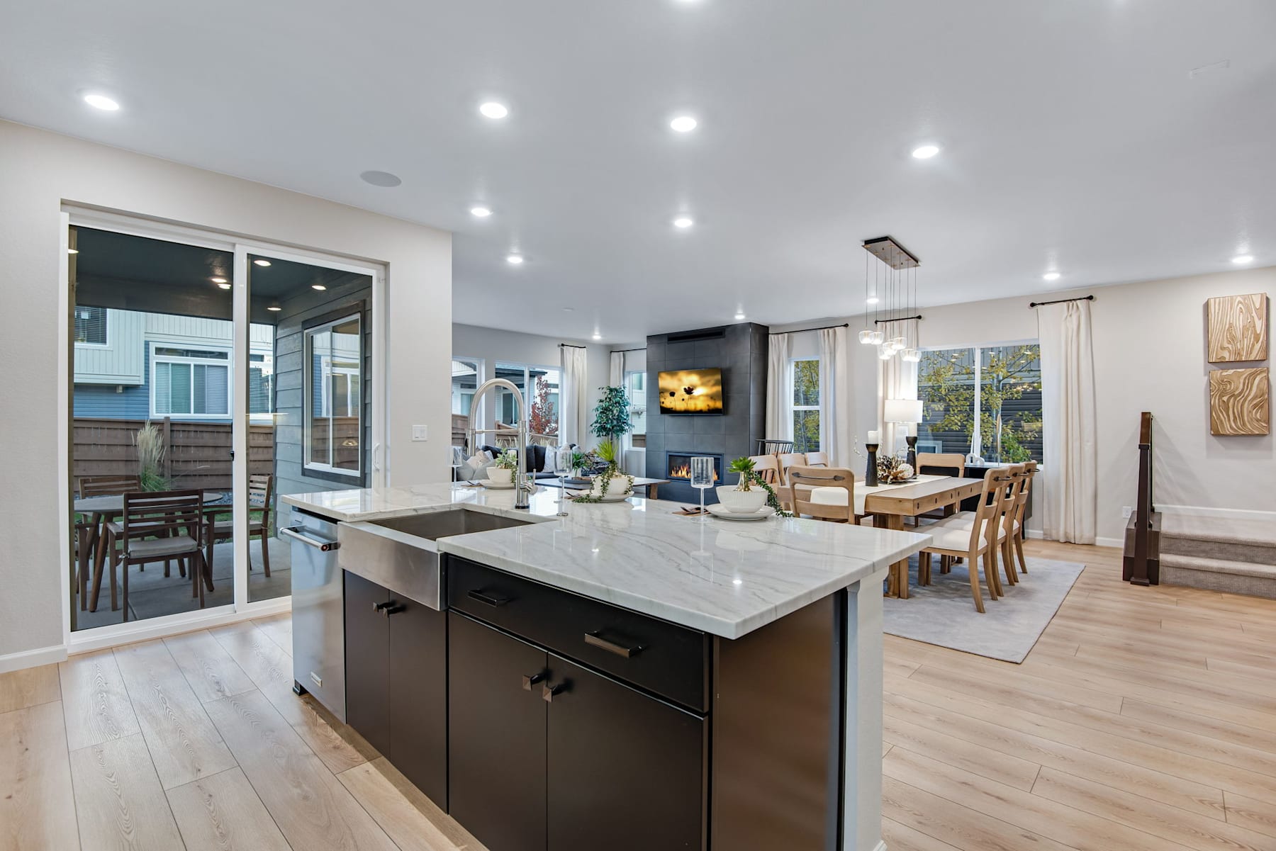 A modern, open-concept kitchen and living room with a large island, wooden floors, and a TV mounted on the wall.