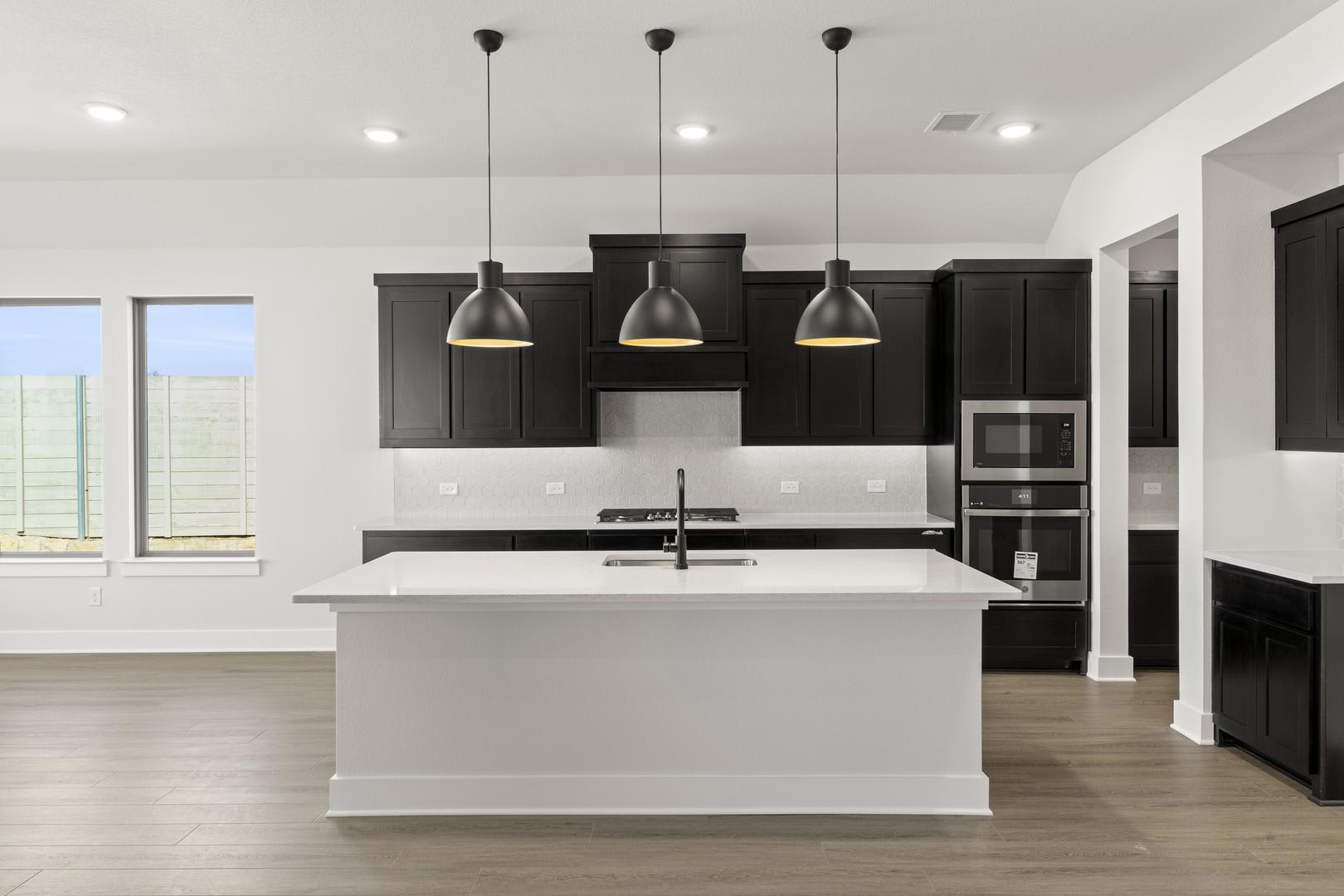 A modern, minimalist kitchen with a white island, black cabinets, and three pendant lights hanging above the counter.