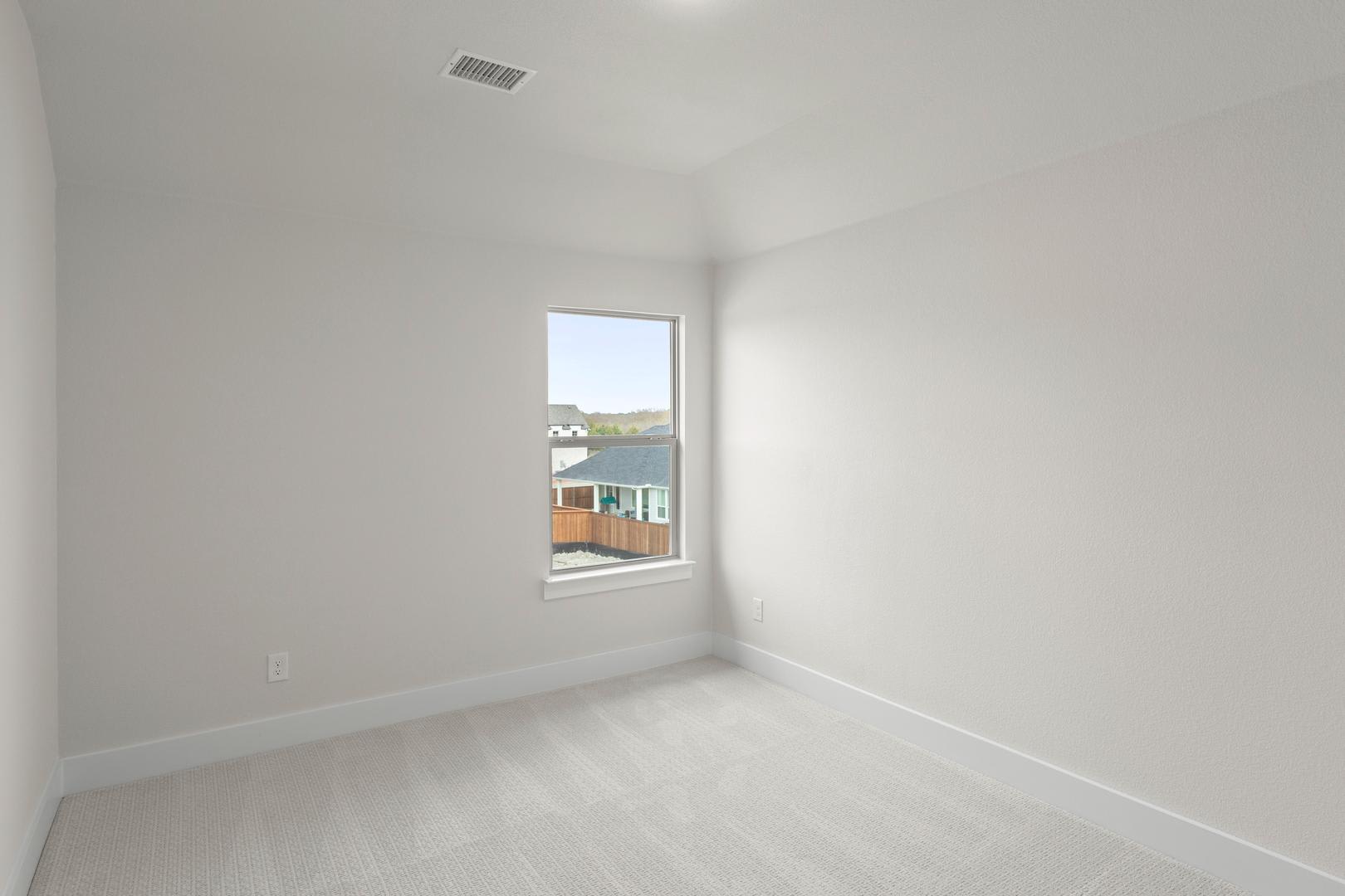 A bright, empty room with a window overlooking a residential area in the background.
