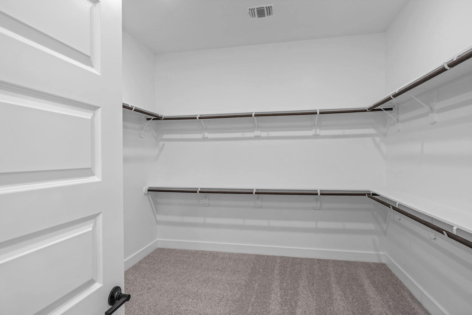 A spacious, well-lit walk-in closet with multiple shelves and hanging rods, providing ample storage space.