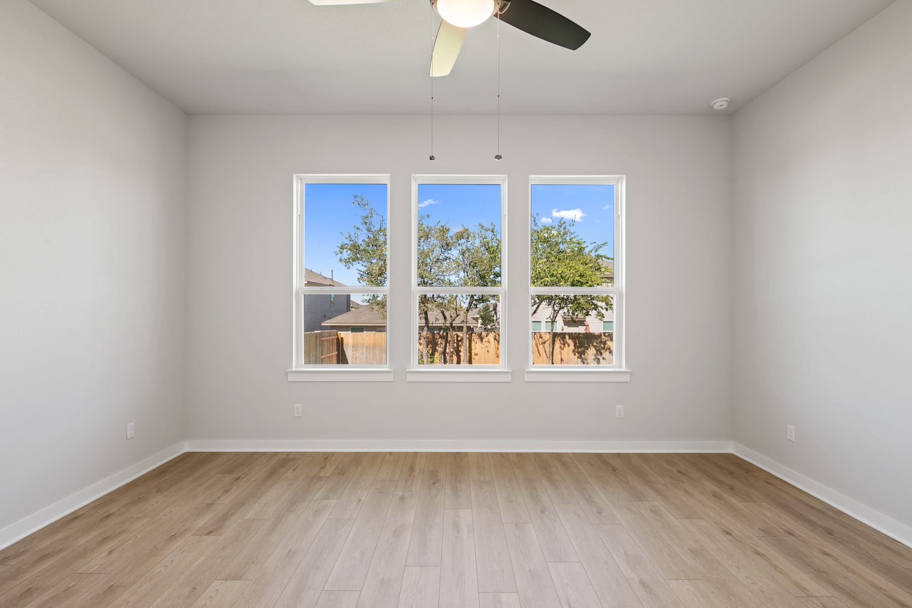 A bright and airy room with large windows overlooking a lush outdoor landscape, featuring a ceiling fan and hardwood flooring.