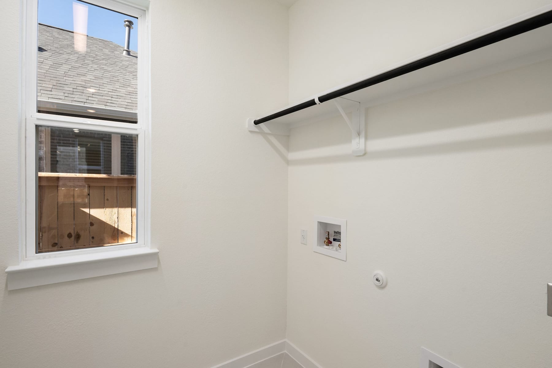A small, well-lit room with a window, a wooden door, and a hanging rod for storage.