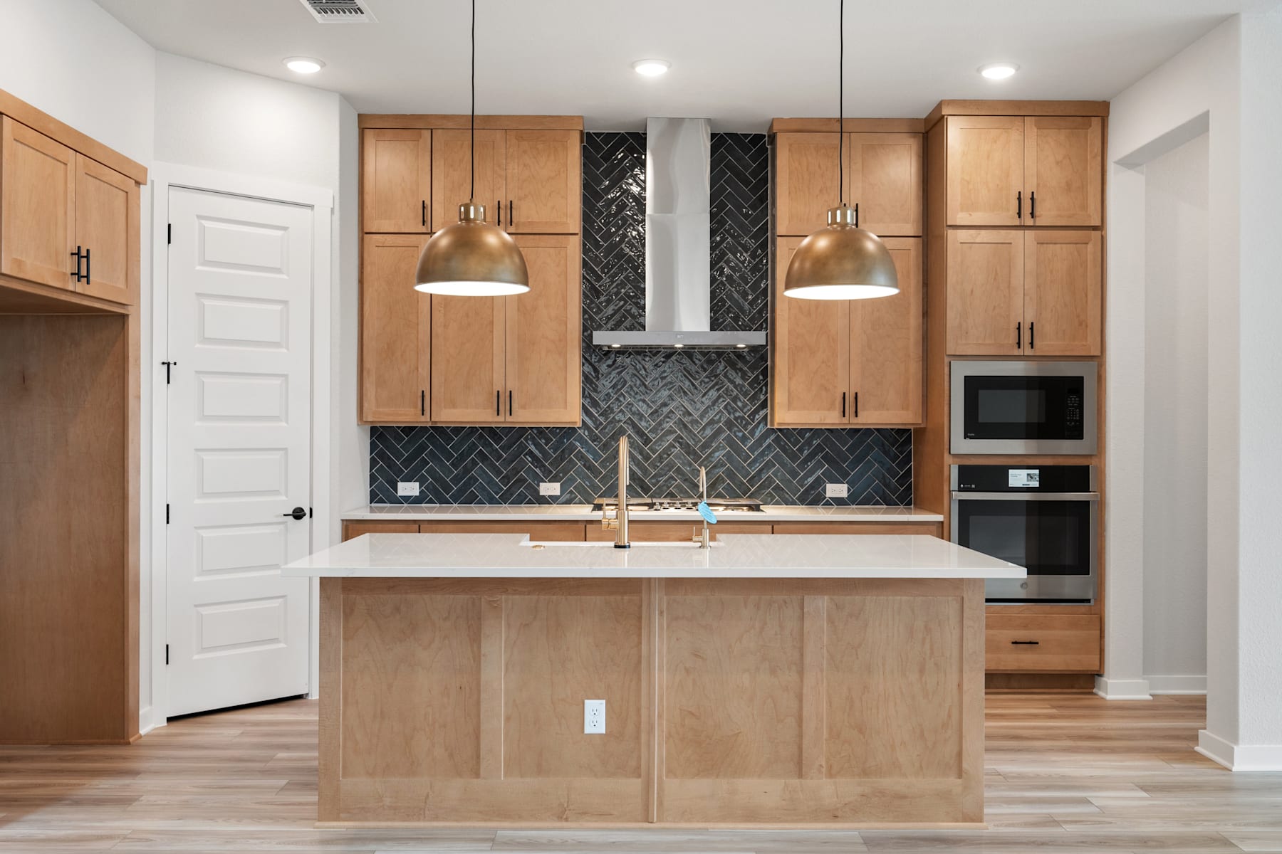 A modern and minimalist kitchen with light wood cabinets, a central island, and a patterned backsplash, creating a warm and inviting atmosphere.