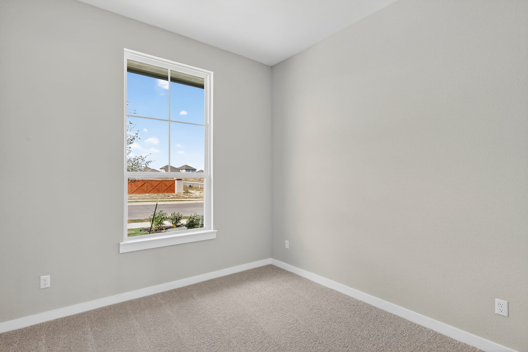 A bright and airy room with a large window overlooking a residential neighborhood, featuring a wooden shelf on the wall and a carpeted floor.