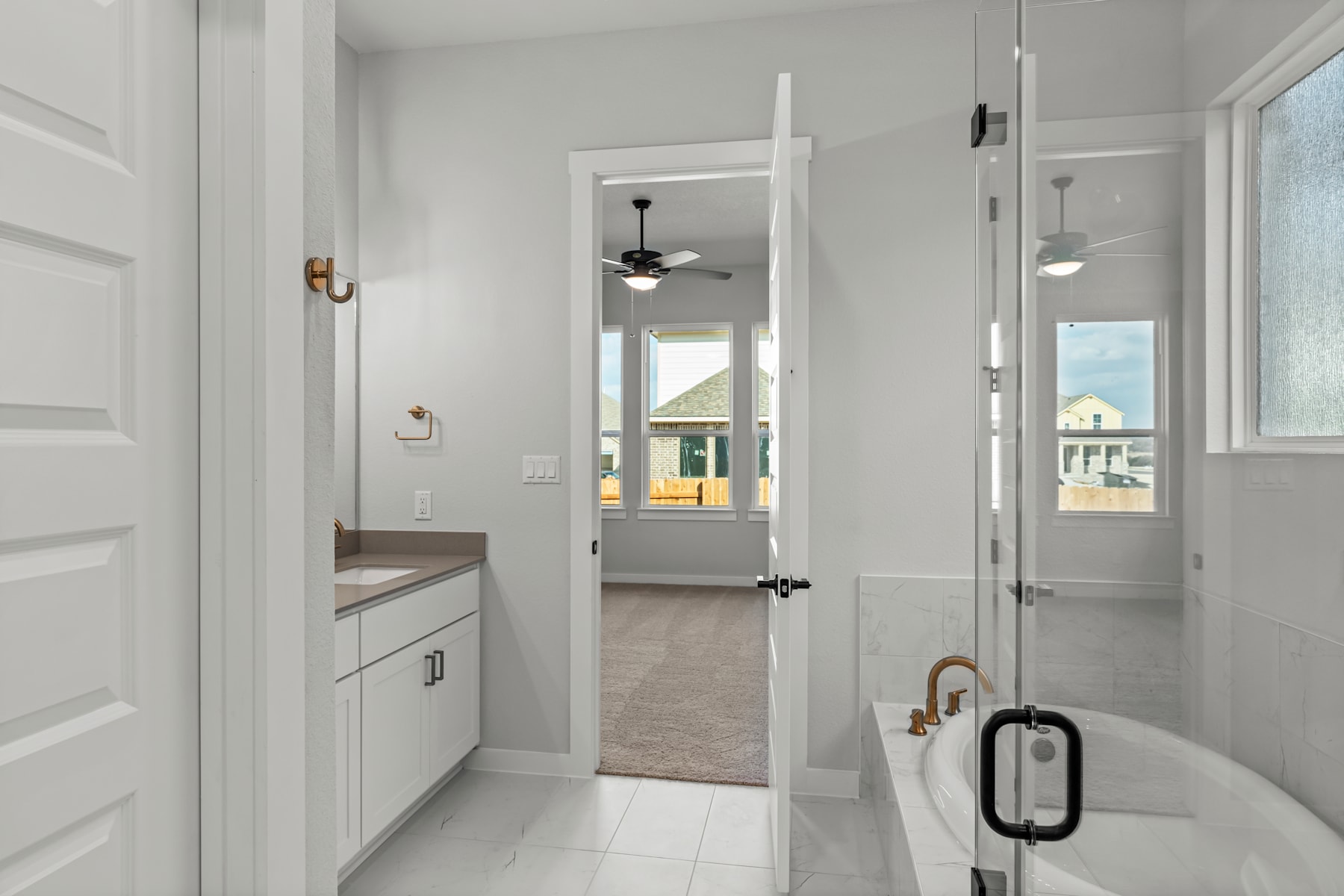 A modern, well-lit bathroom with a white vanity, a freestanding bathtub, and a doorway leading to another room.