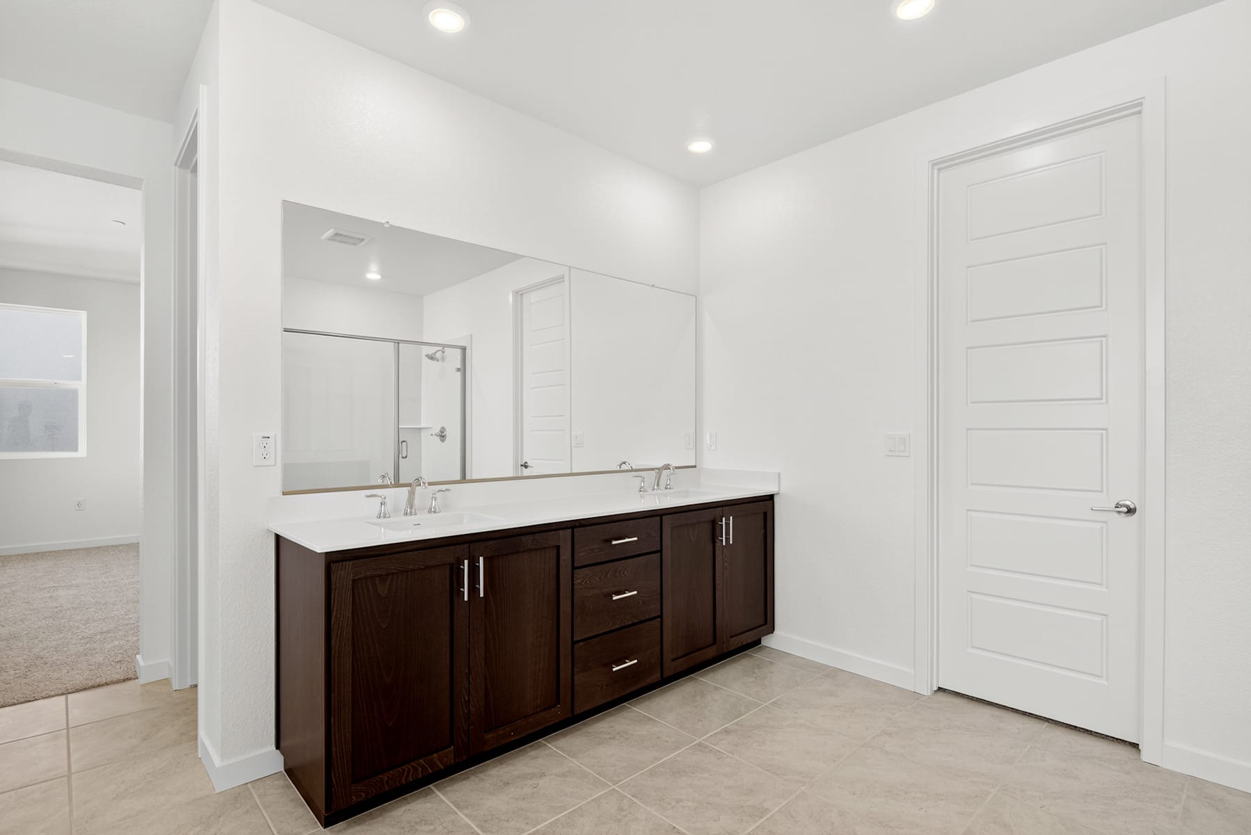 A modern, minimalist bathroom with a large vanity cabinet in a dark wood finish, a large mirror, and a tiled floor.
