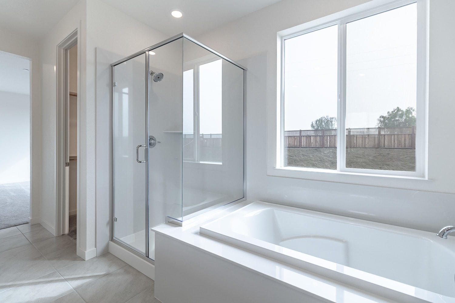 A modern, bright bathroom with a large window, a glass-enclosed shower, and a white bathtub.
