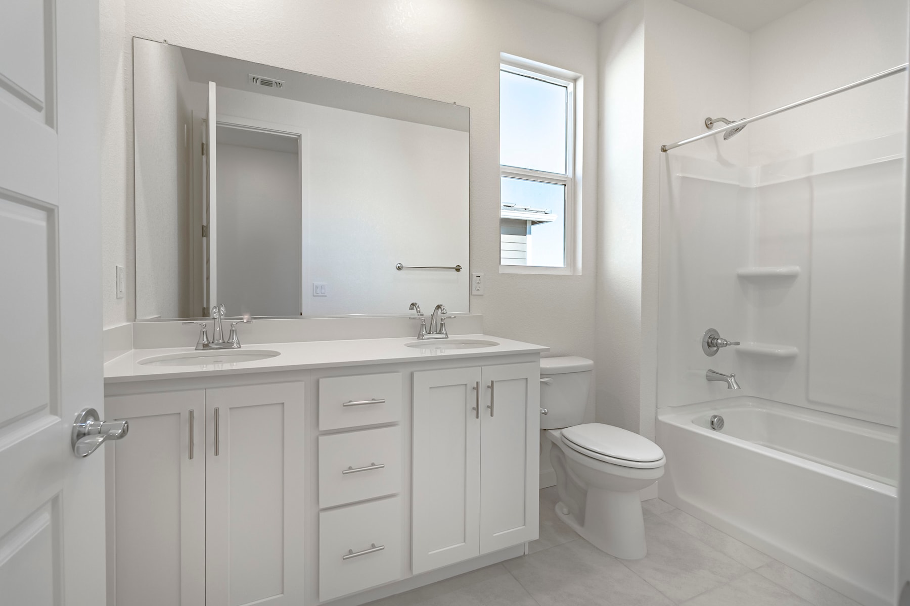 A modern, well-lit bathroom with a vanity, mirror, and a bathtub surrounded by white walls and tile flooring.