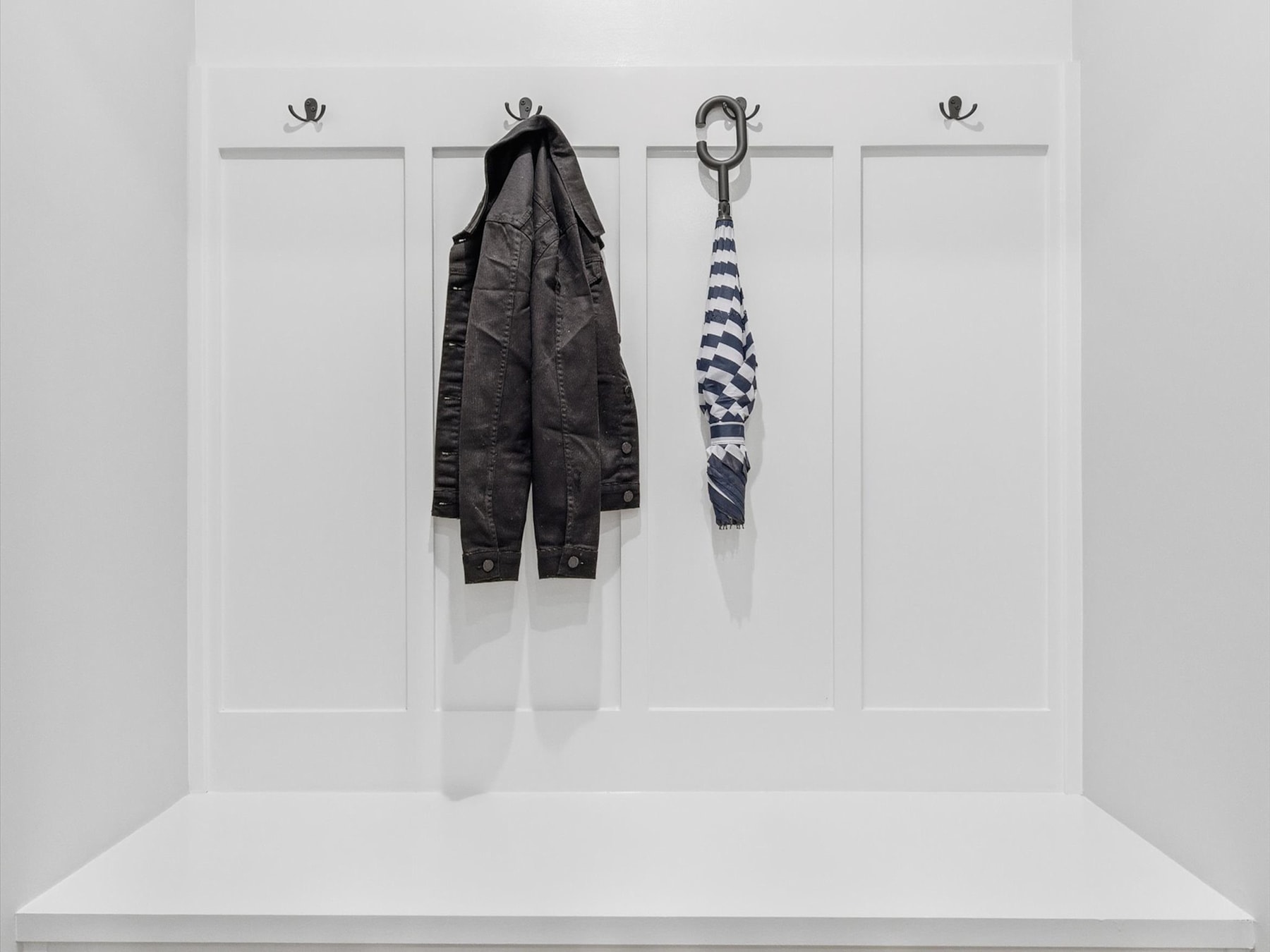 A minimalist white wall with four hooks, each holding a different black and white garment or accessory, creating a simple and organized display.