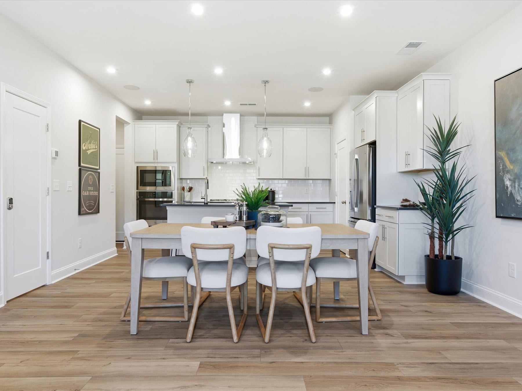 A modern, open-concept kitchen and dining area with white cabinets, stainless steel appliances, and a wooden dining table with chairs.