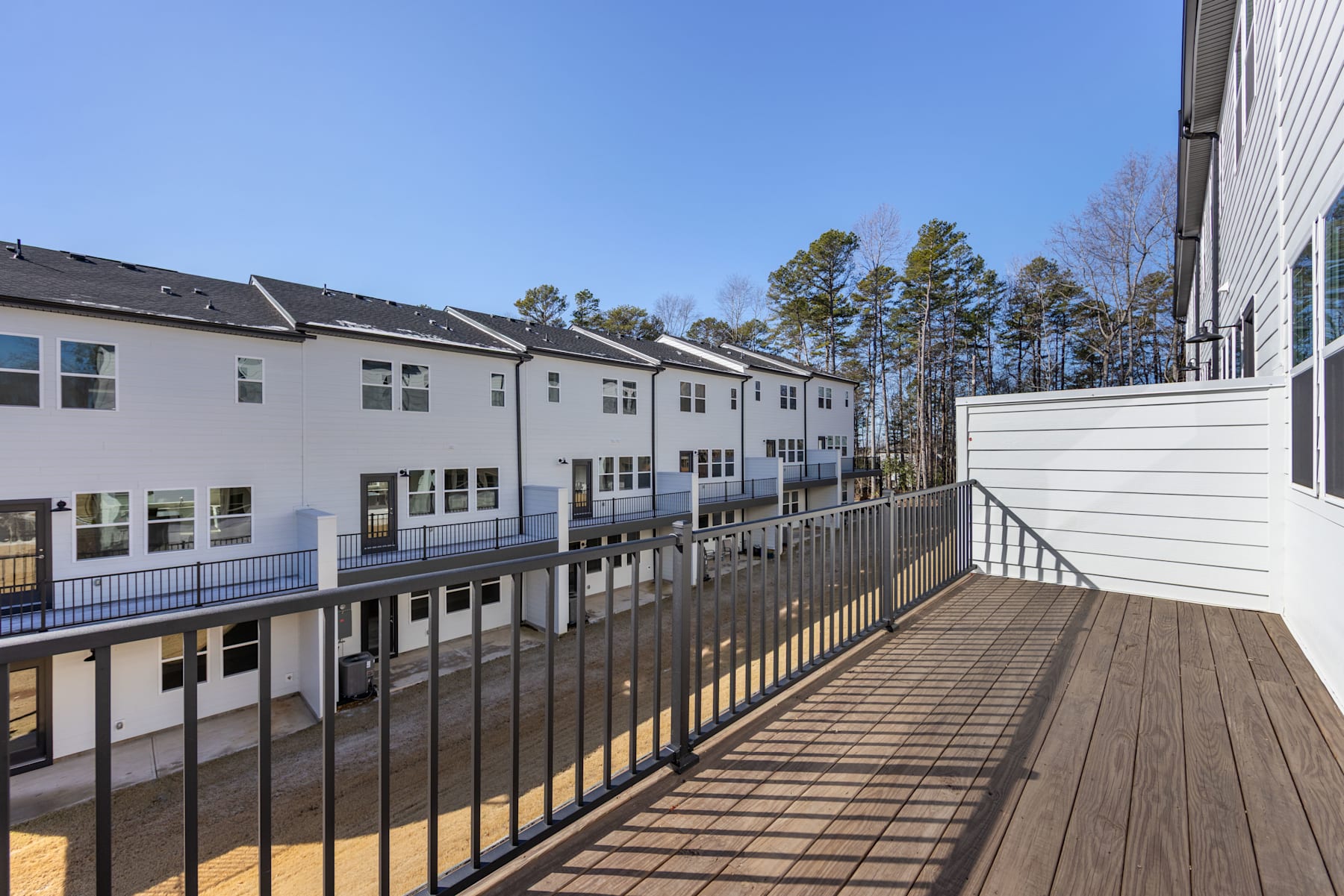 A multi-story residential building with a wooden deck and railing overlooking a wooded area in the background.