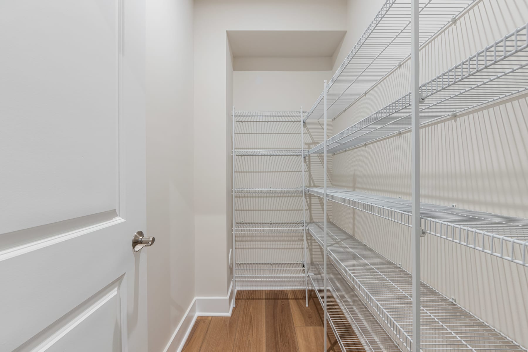 A well-organized and spacious walk-in closet with white walls, wire shelving units, and a wooden floor.