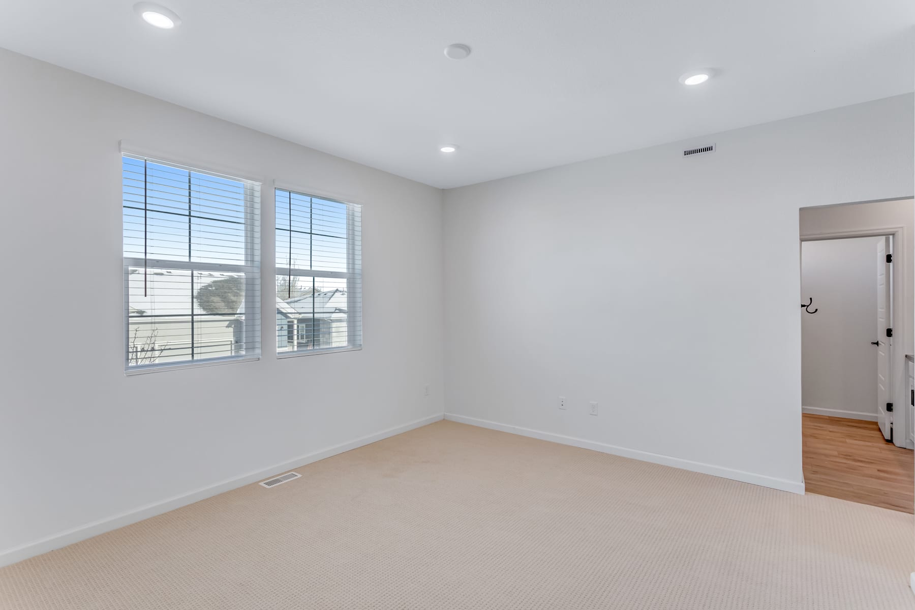 An empty, well-lit room with large windows, hardwood floors, and a neutral color scheme.
