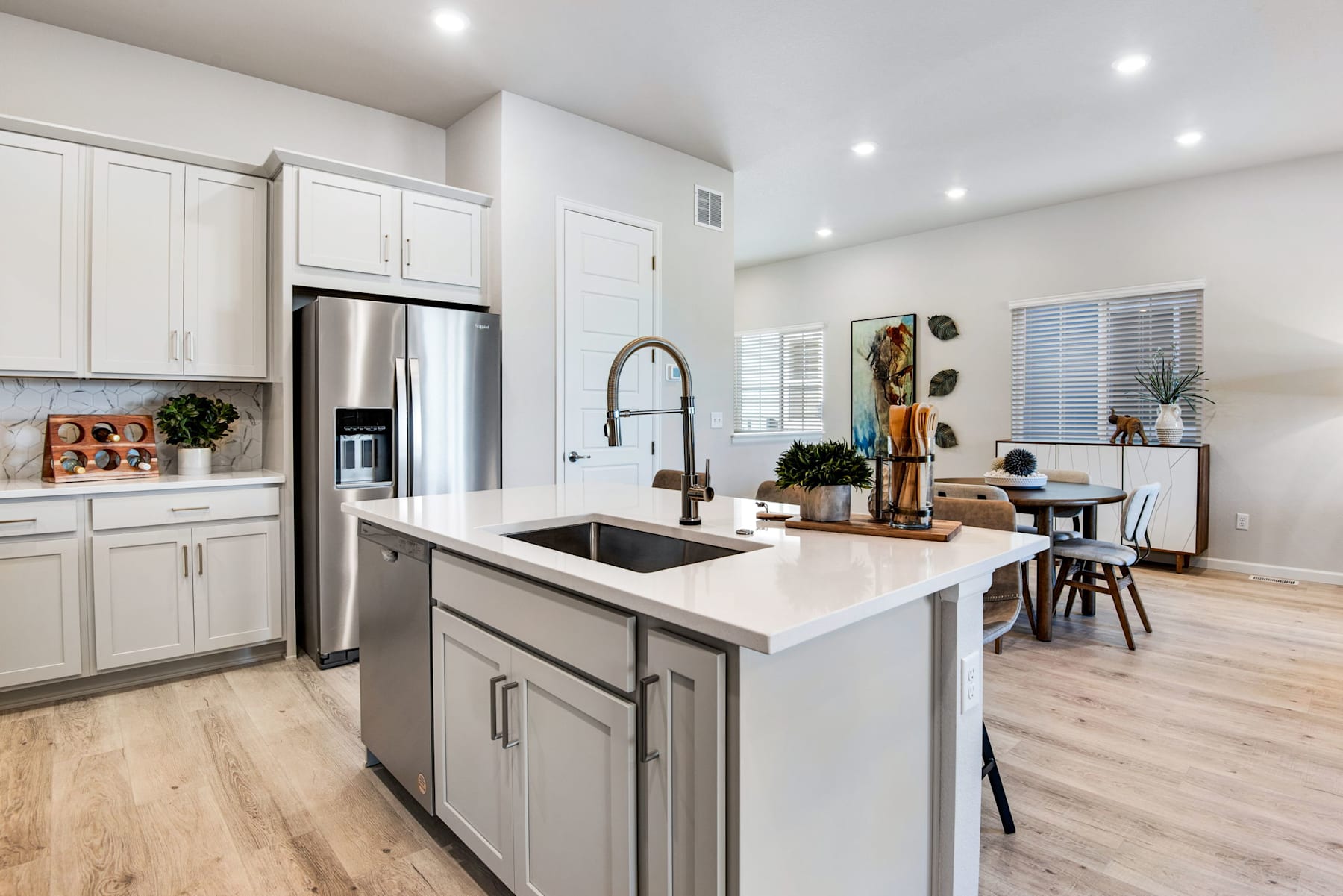 A modern, open-concept kitchen with white cabinets, a large island, and a dining area visible in the background.