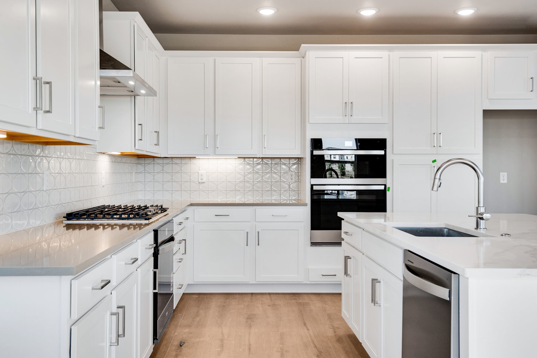 A modern, well-equipped kitchen with white cabinets, stainless steel appliances, and a tiled backsplash, set against a hardwood floor.