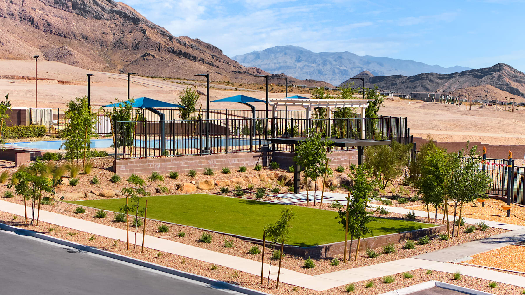 A well-designed outdoor recreational area with a lush green lawn, shaded seating areas, and a basketball court, set against the backdrop of rugged, mountainous terrain.