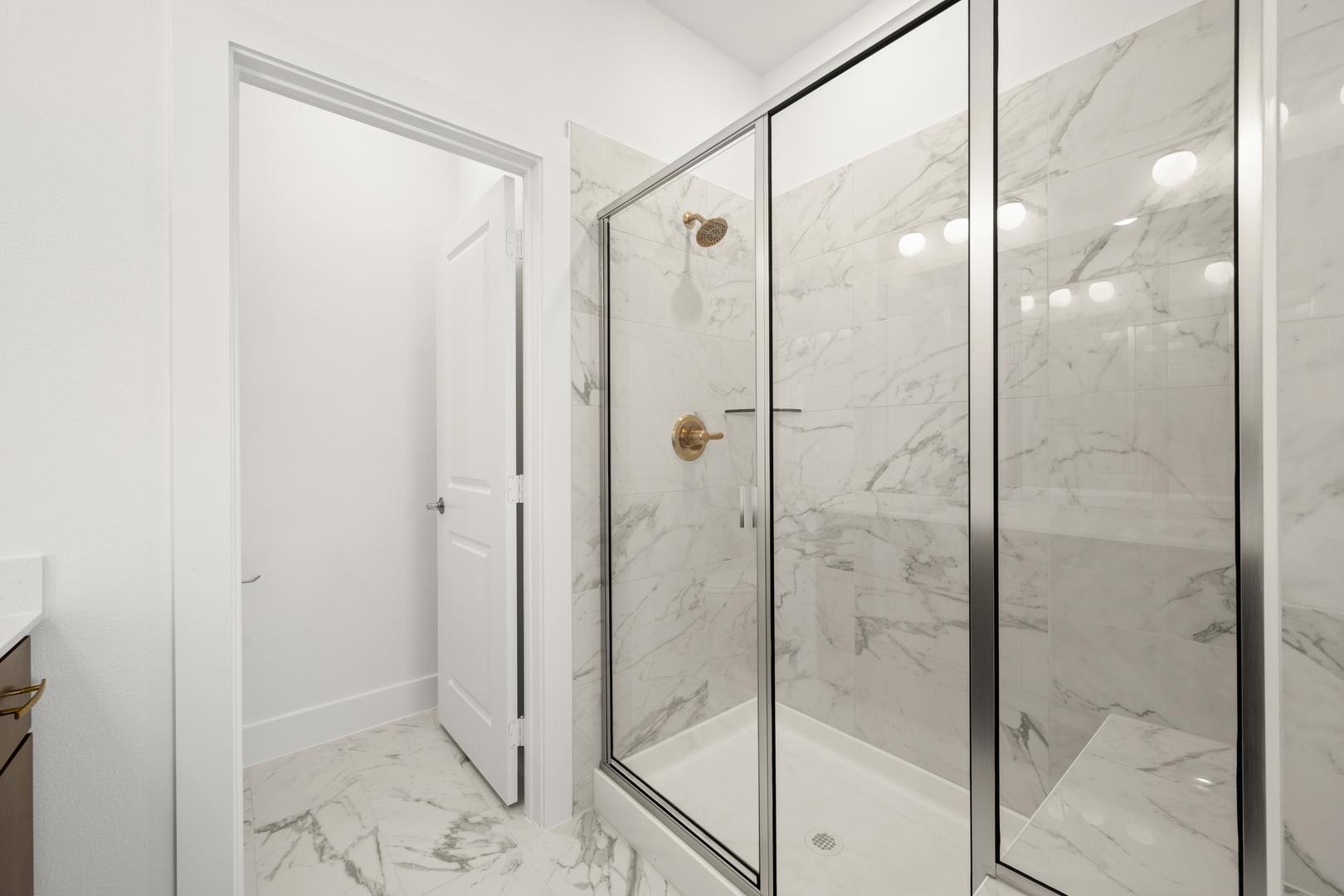 A modern, minimalist bathroom with a glass-enclosed shower and marble-like tiles covering the walls and floor.