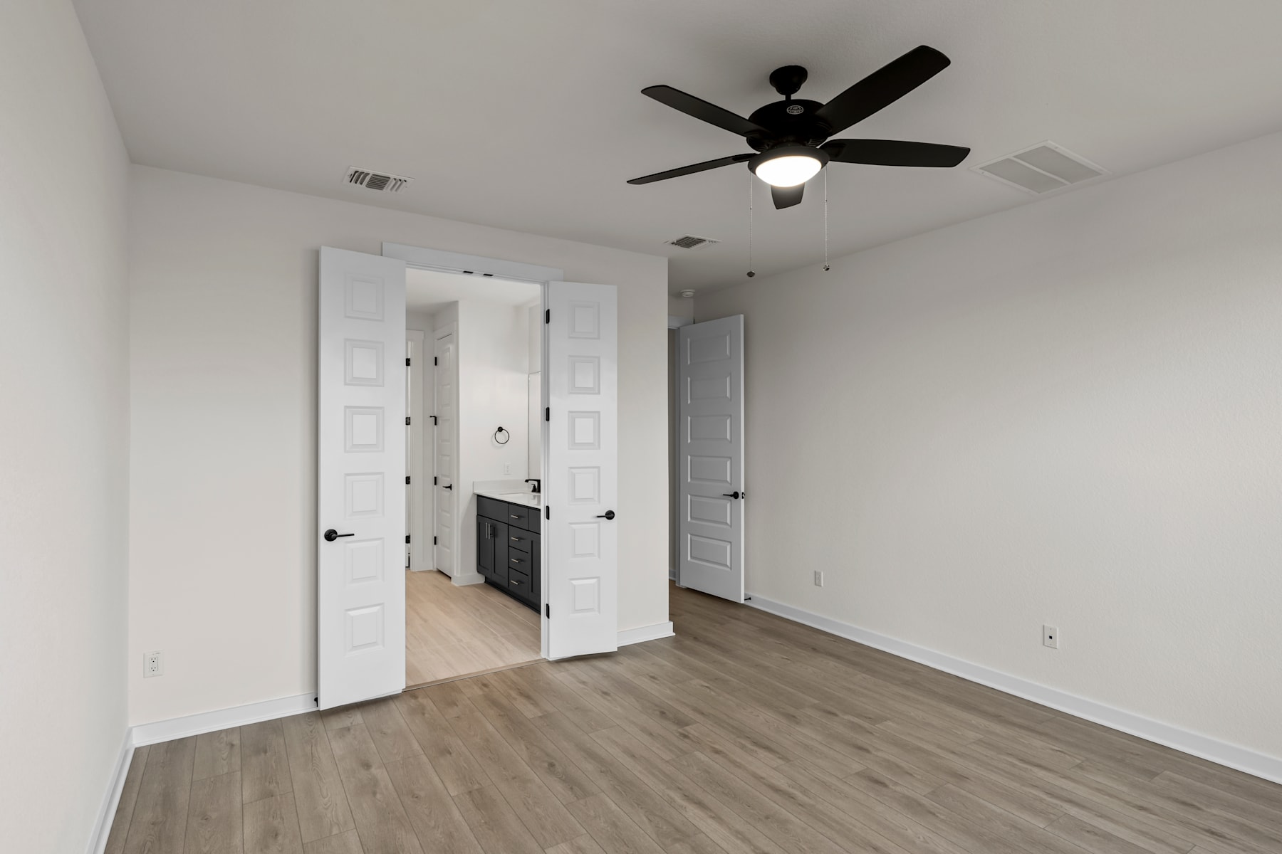 A sparsely furnished room with a ceiling fan, white doors, and a hardwood floor.