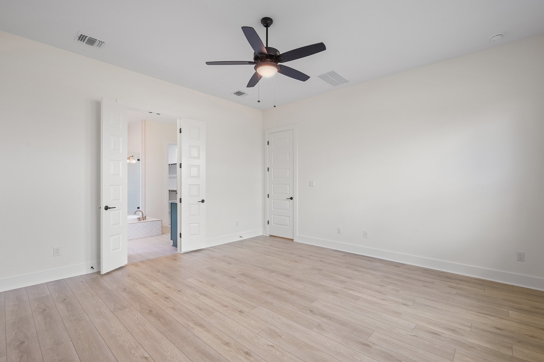 An empty room with a ceiling fan, white walls, and hardwood flooring.