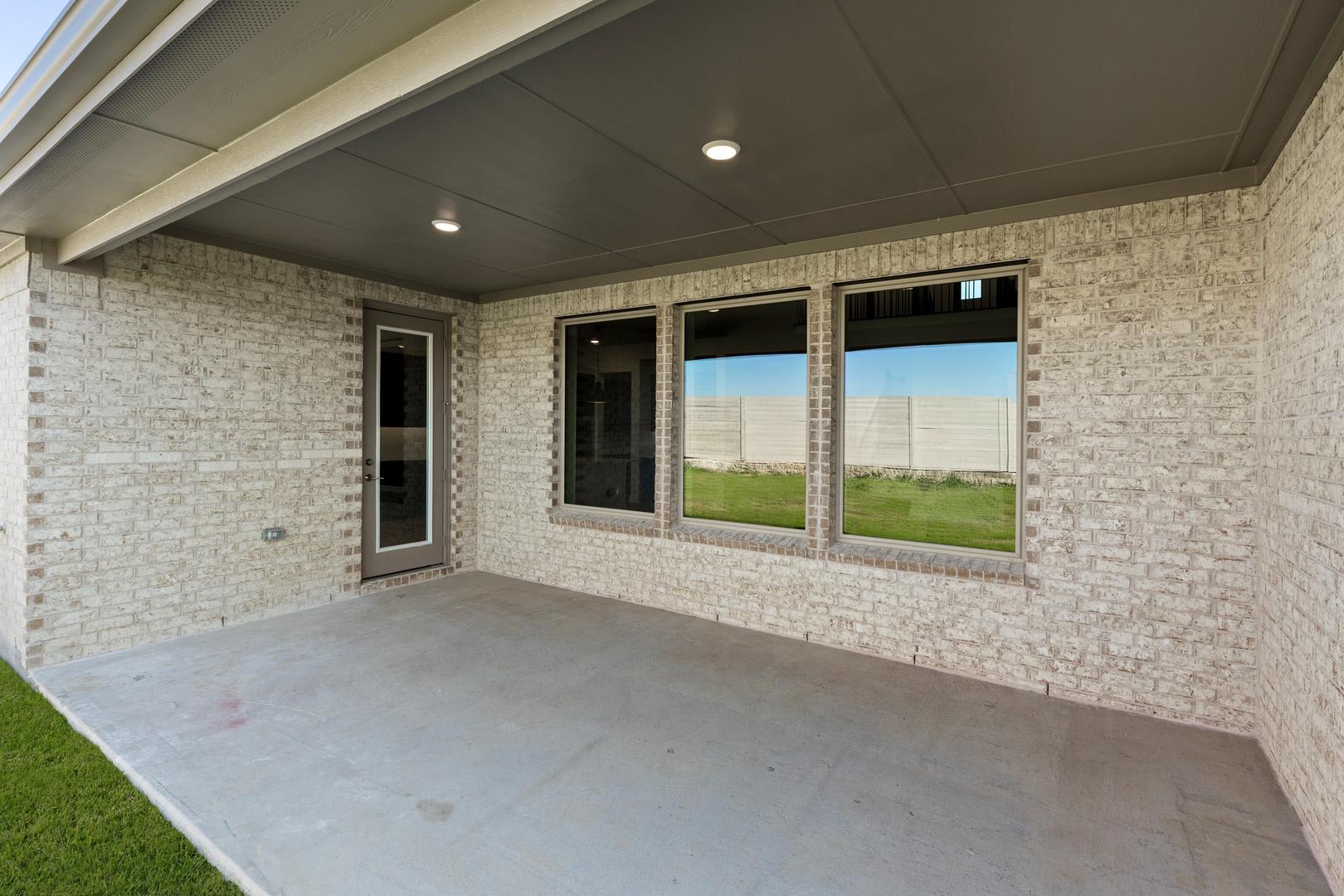 A covered patio with large windows overlooking a grassy outdoor area.