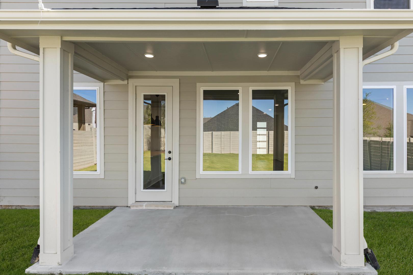 A modern, well-lit entryway with a covered porch, surrounded by a grassy lawn and a clear sky in the background.
