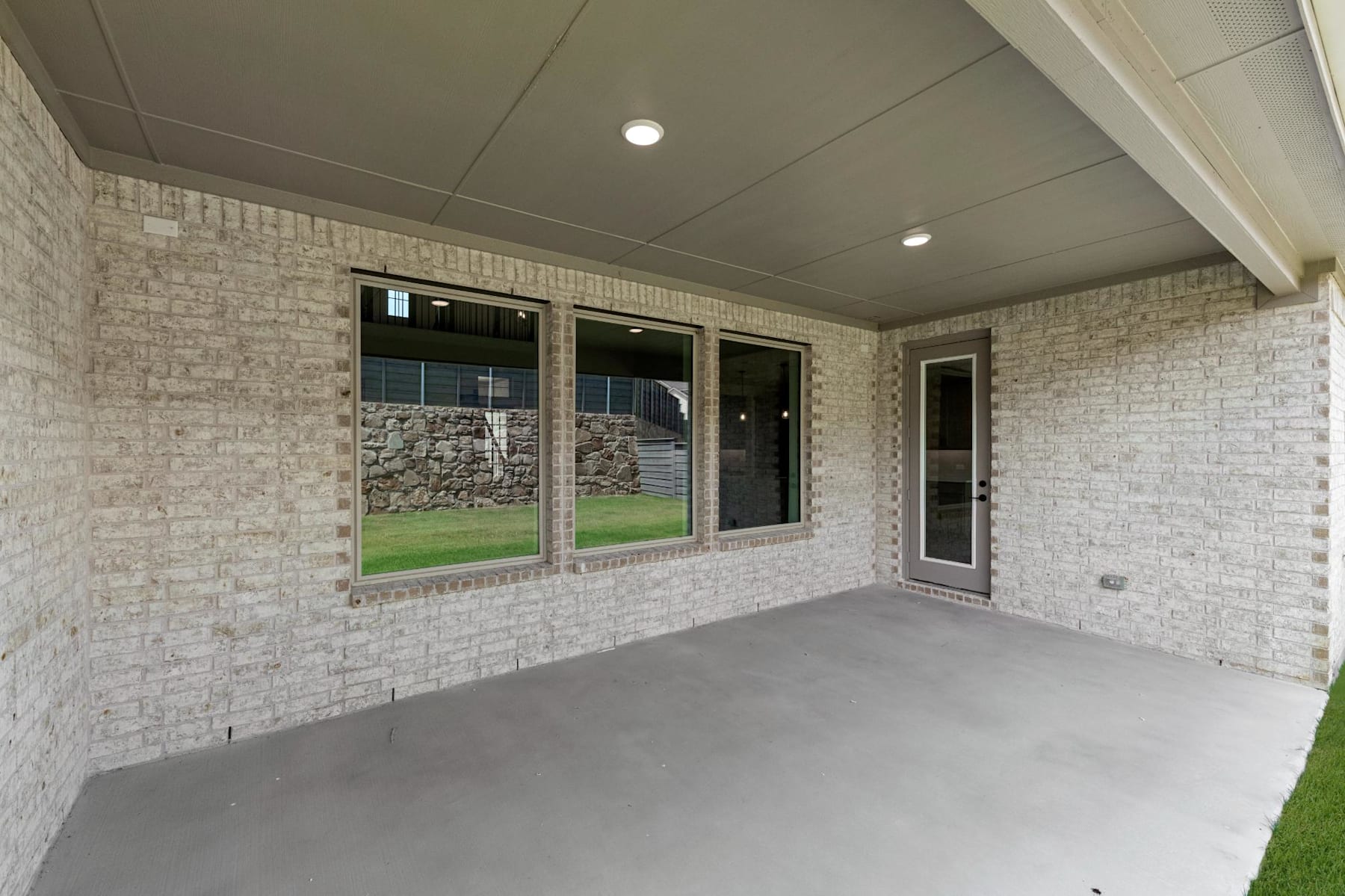 A spacious porch with a tiled ceiling, recessed lighting, and large windows overlooking a grassy outdoor area.