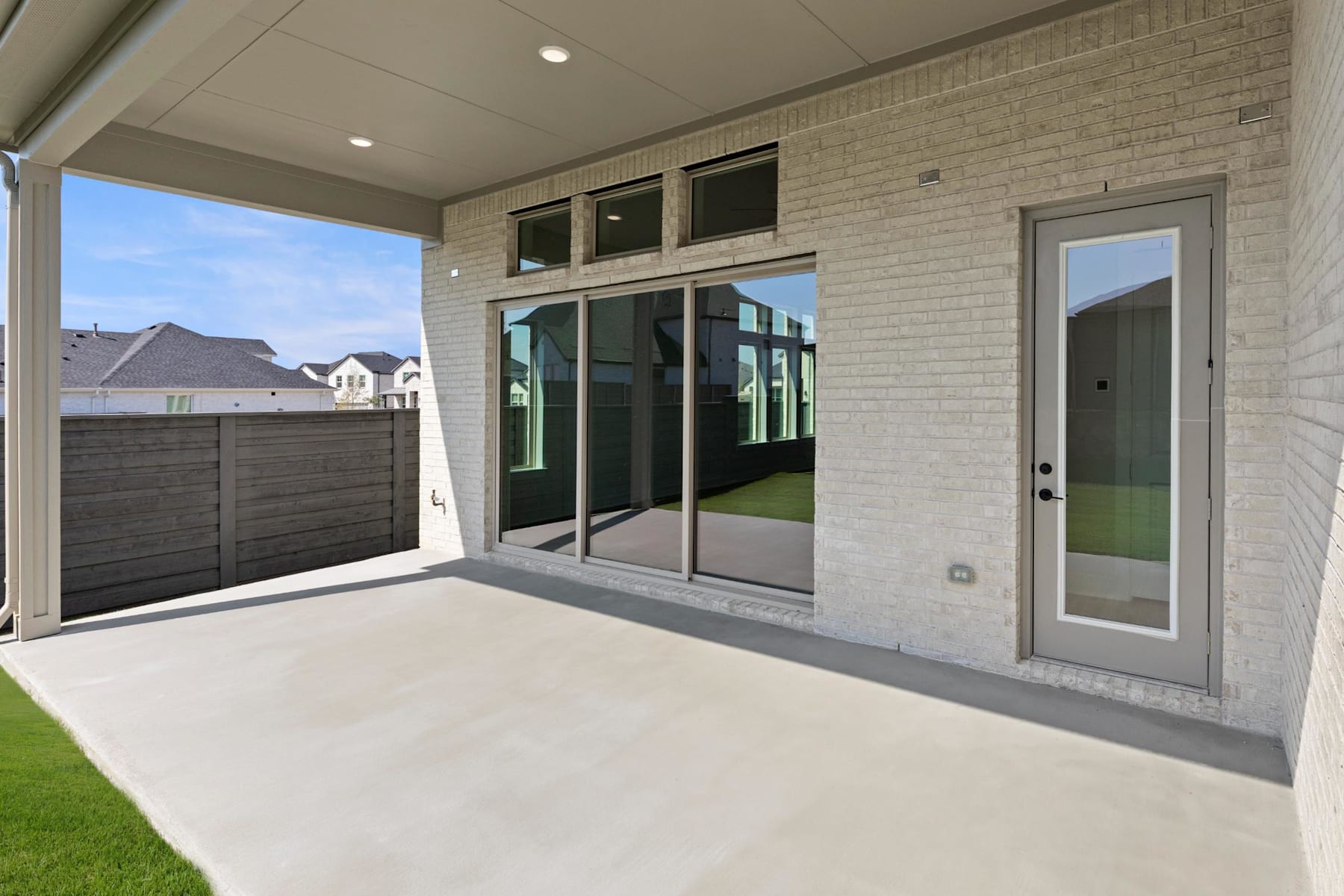 A modern, well-lit patio with a brick exterior, large sliding glass doors, and a grassy yard visible in the background.