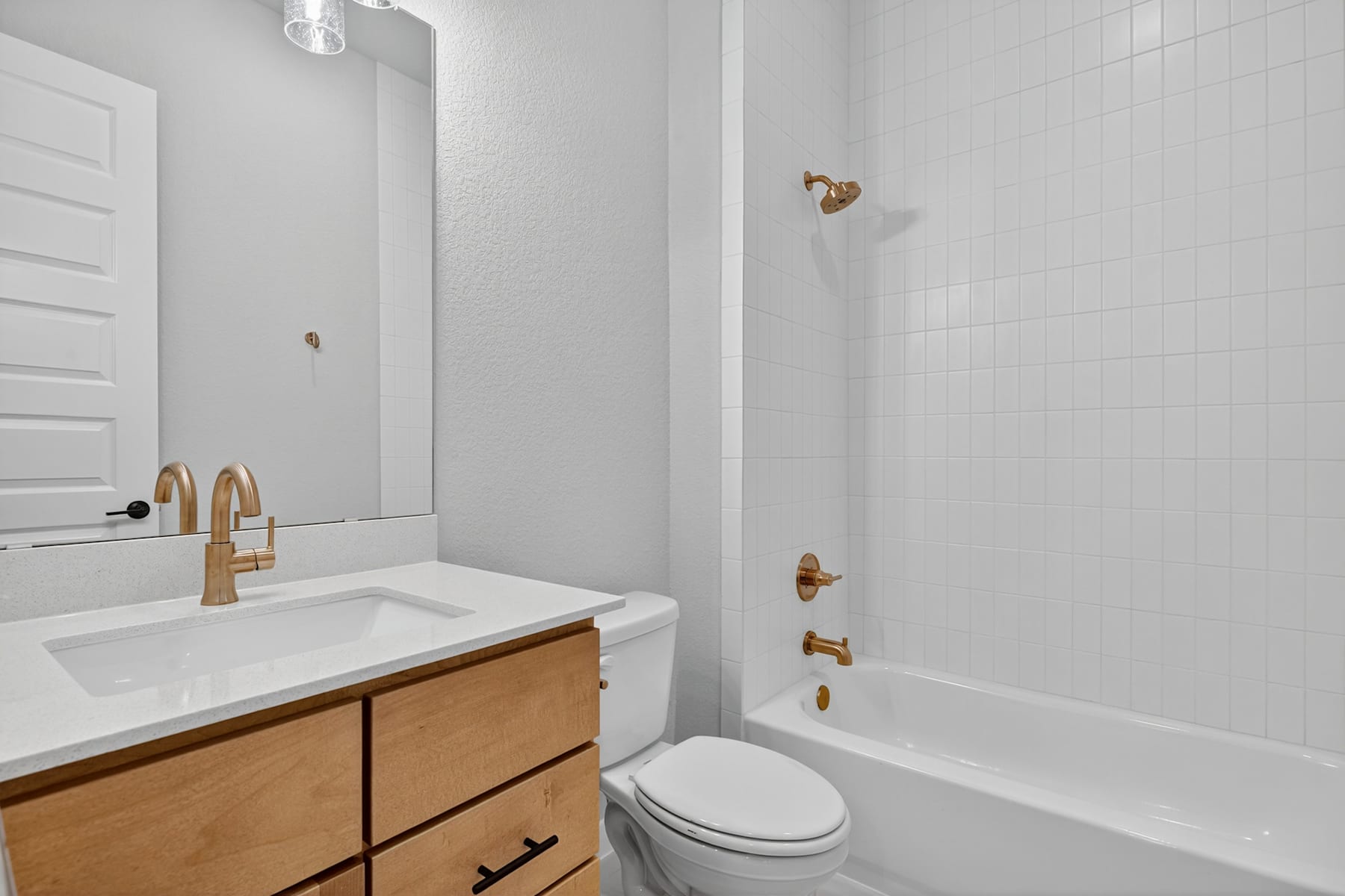 A modern bathroom with a white vanity, gold fixtures, and a tiled shower enclosure.