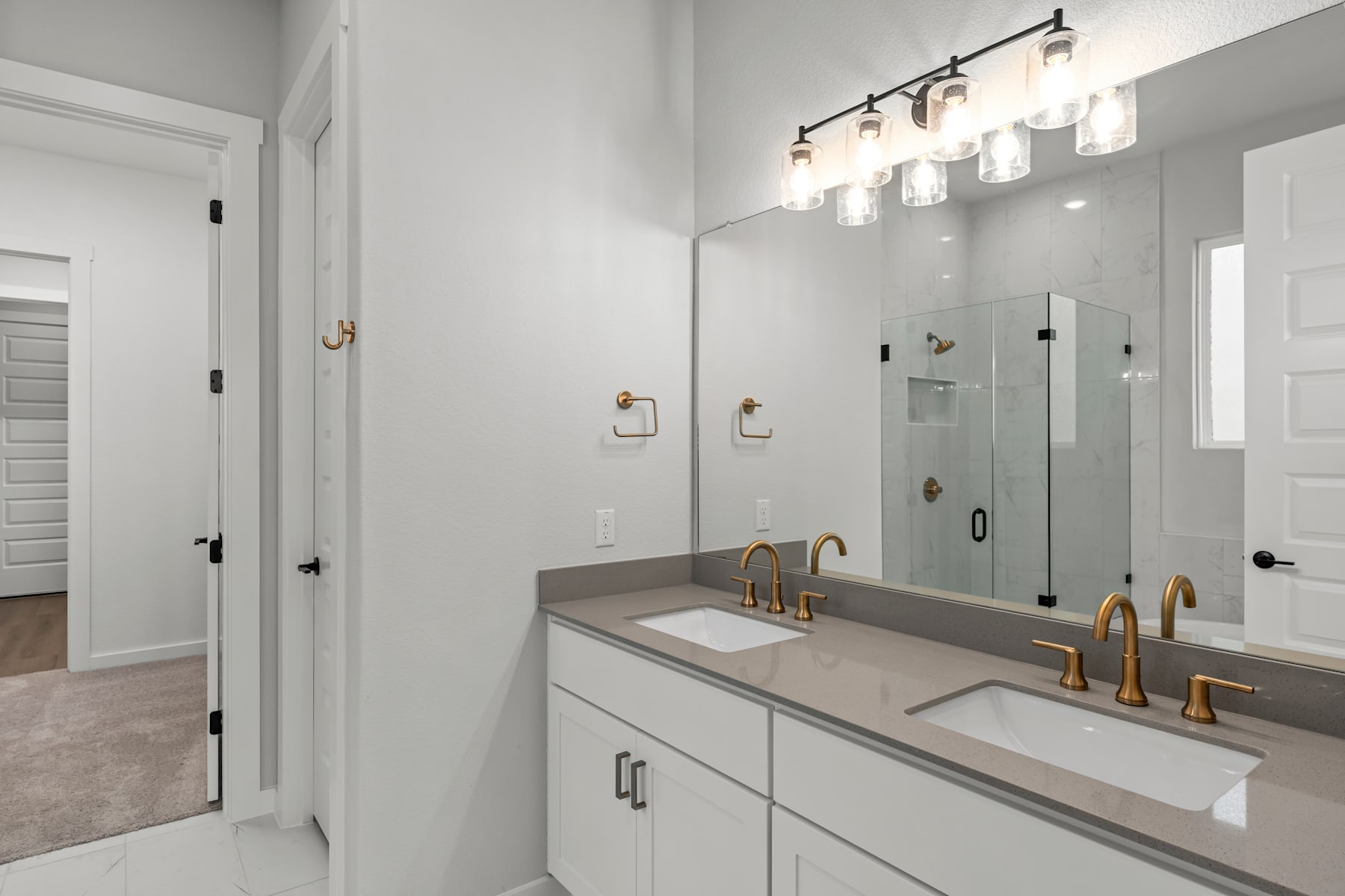 A modern and well-lit bathroom with a double vanity, a large mirror, and a glass shower enclosure, featuring a sleek and minimalist design.