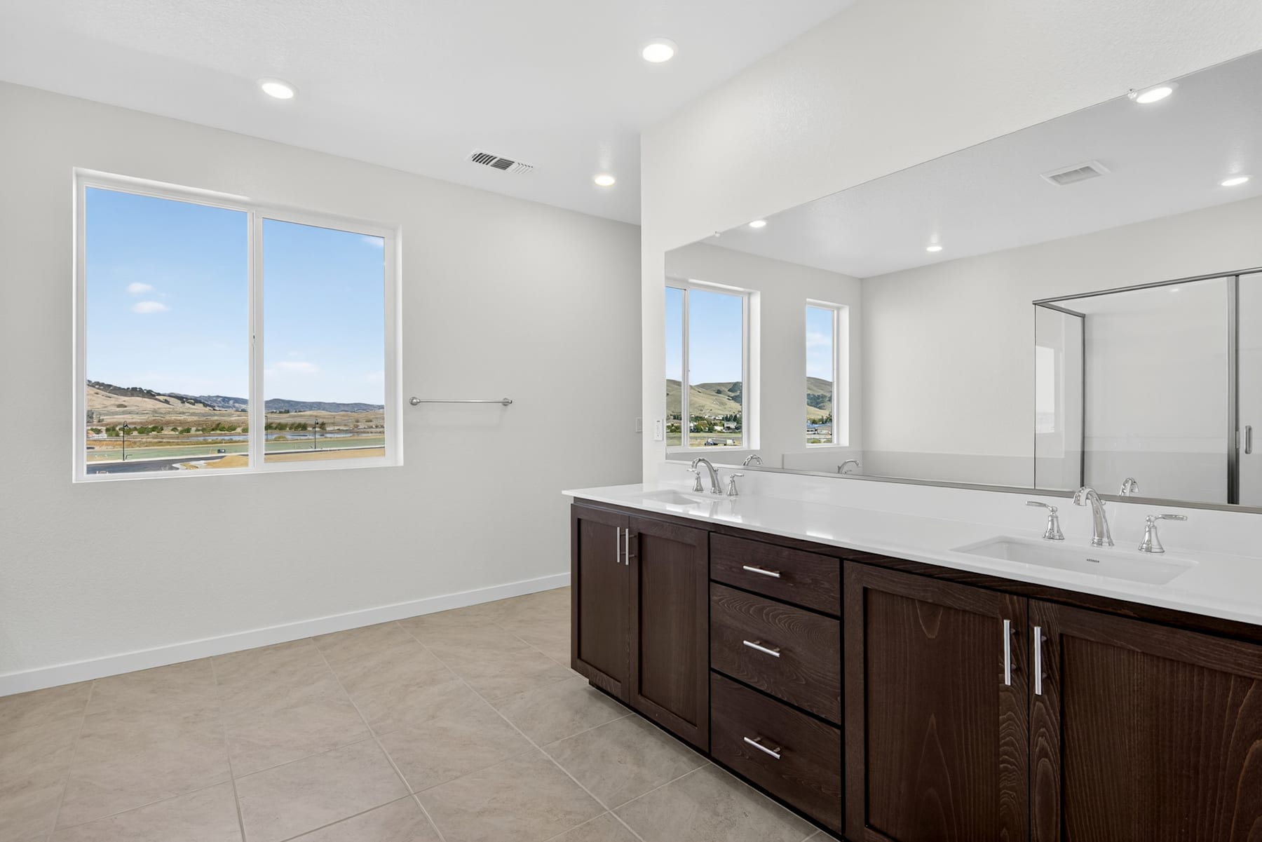 A modern and spacious bathroom with a large vanity, double sinks, and large windows overlooking a scenic outdoor landscape.