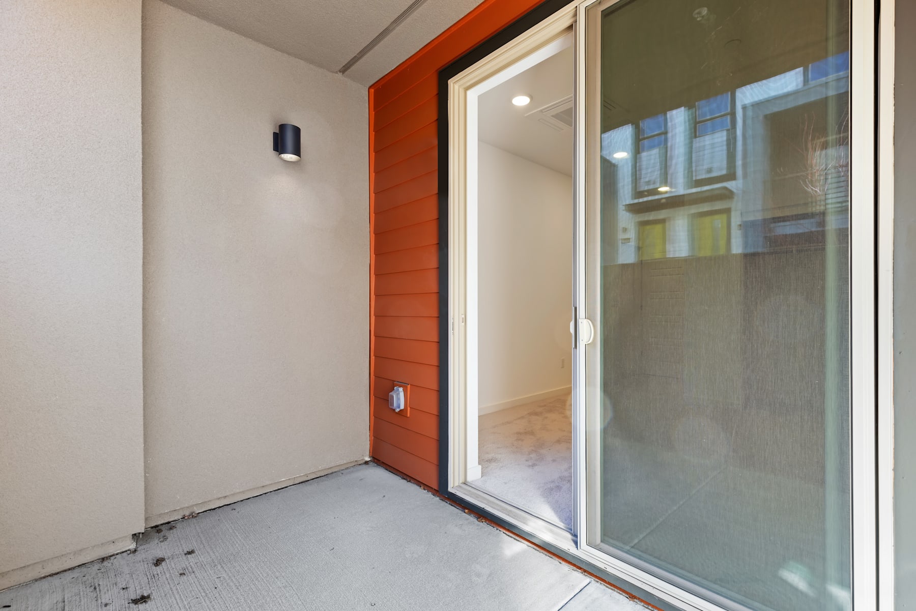 The image shows a modern, minimalist entryway with a red wooden door, a glass sliding door, and a white wall in the background.