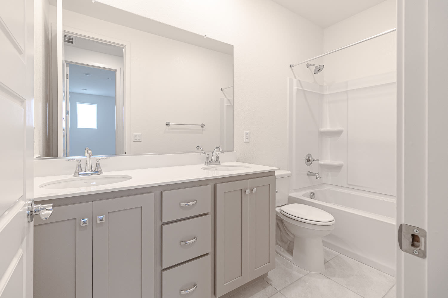 A modern, clean bathroom with a gray vanity, white countertop, and a large mirror on the wall.